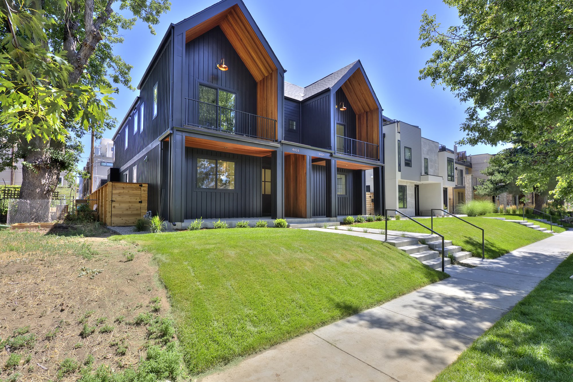 Front of the new Nordic farmhouse duplex in Denver with two black gables lined in wood, covered porches and a green lawn