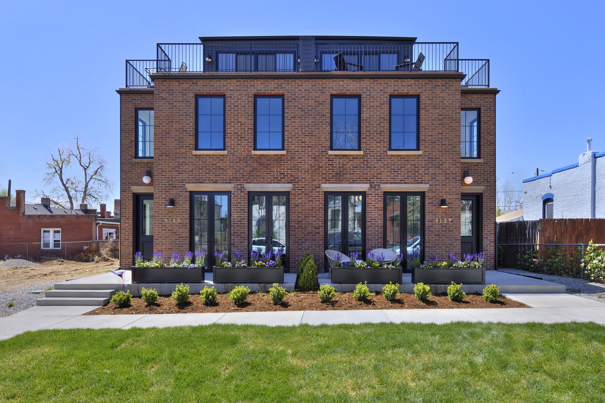 Front of the new custom home in Denver with a red brick facade, black-framed windows and French doors, planter boxes and a lawn
