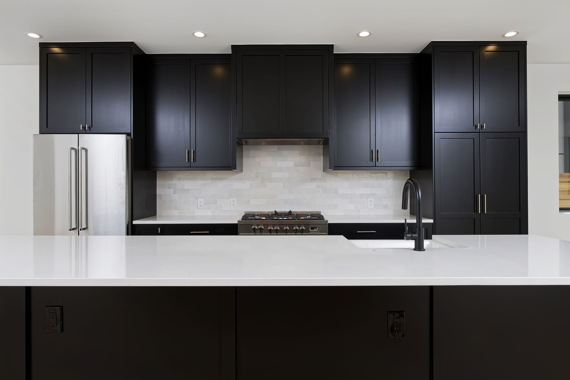 Straight-on view of black cabinets, tile backsplash, stainless range and island