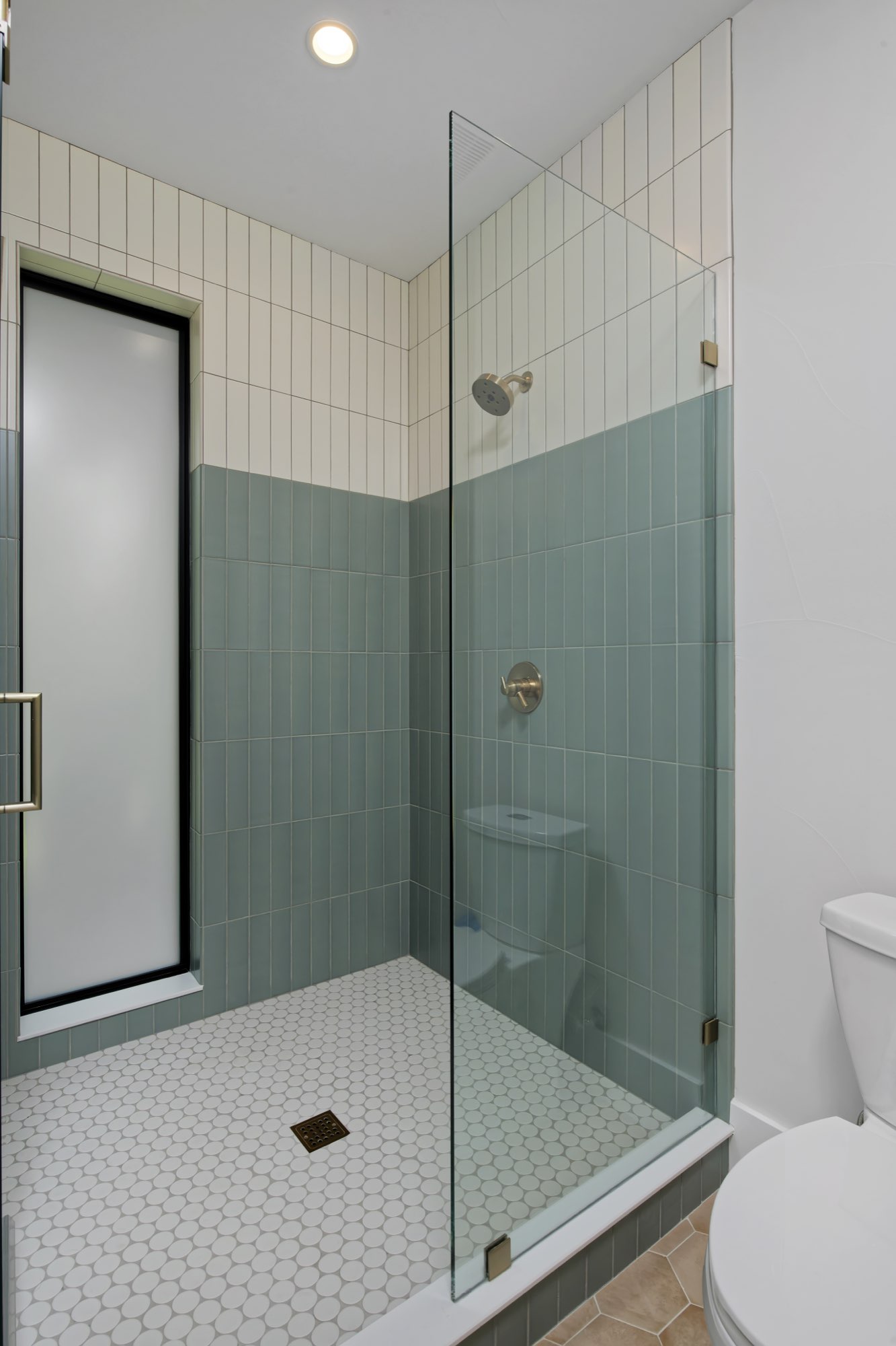 Glass shower with pale green vertical tile, white tile above and a hex tile floor