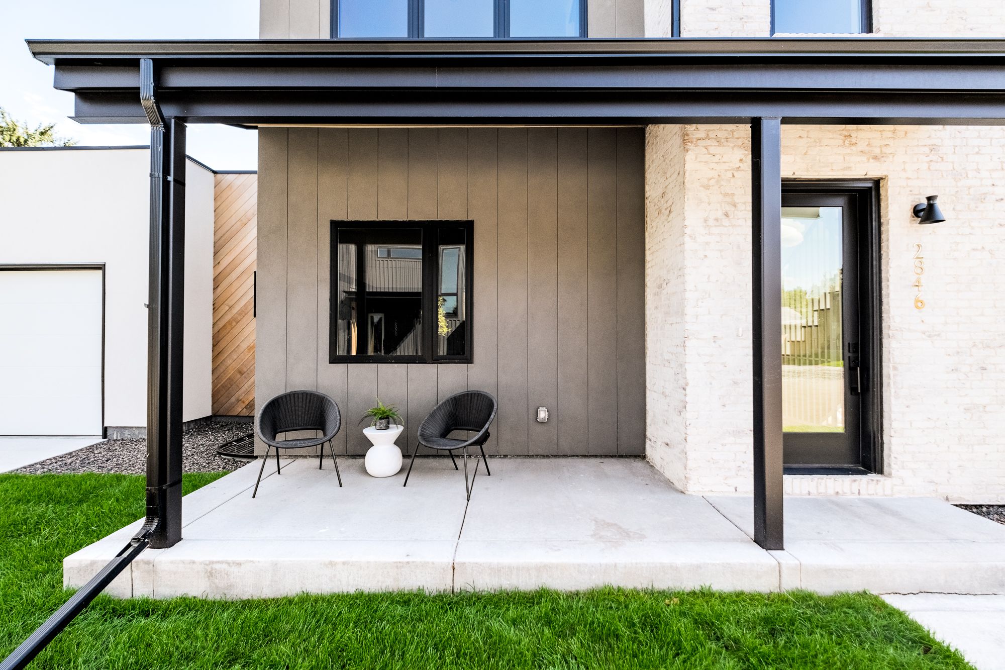 Covered front porch in Wheat Ridge with a black metal porch roof, gray vertical siding and black-framed windows
