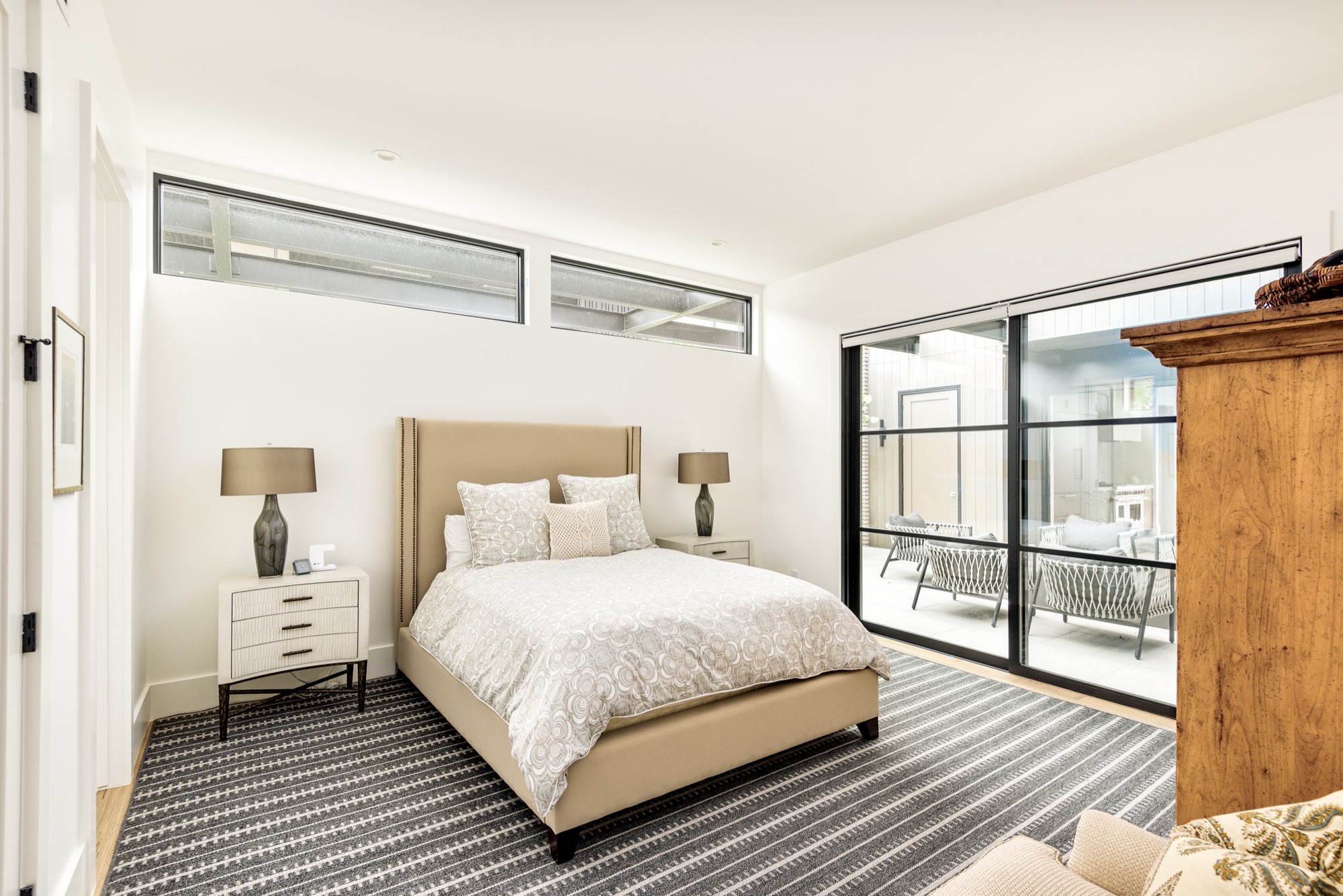 Guest bedroom with high windows, an upholstered bed and black-framed sliding glass doors to the courtyard