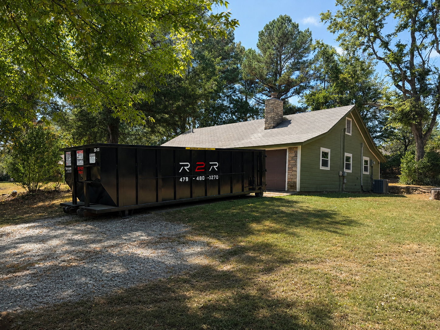 Branded R2R roll-off dumpster set on a gravel driveway beside a Northwest Arkansas home