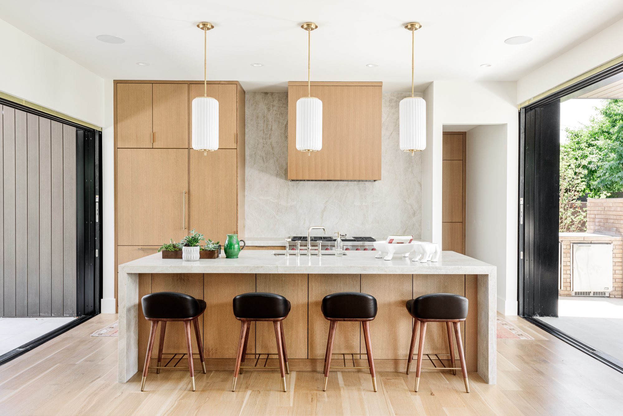 Front of the kitchen island with light wood cabinets, a stone backsplash and three white pendants