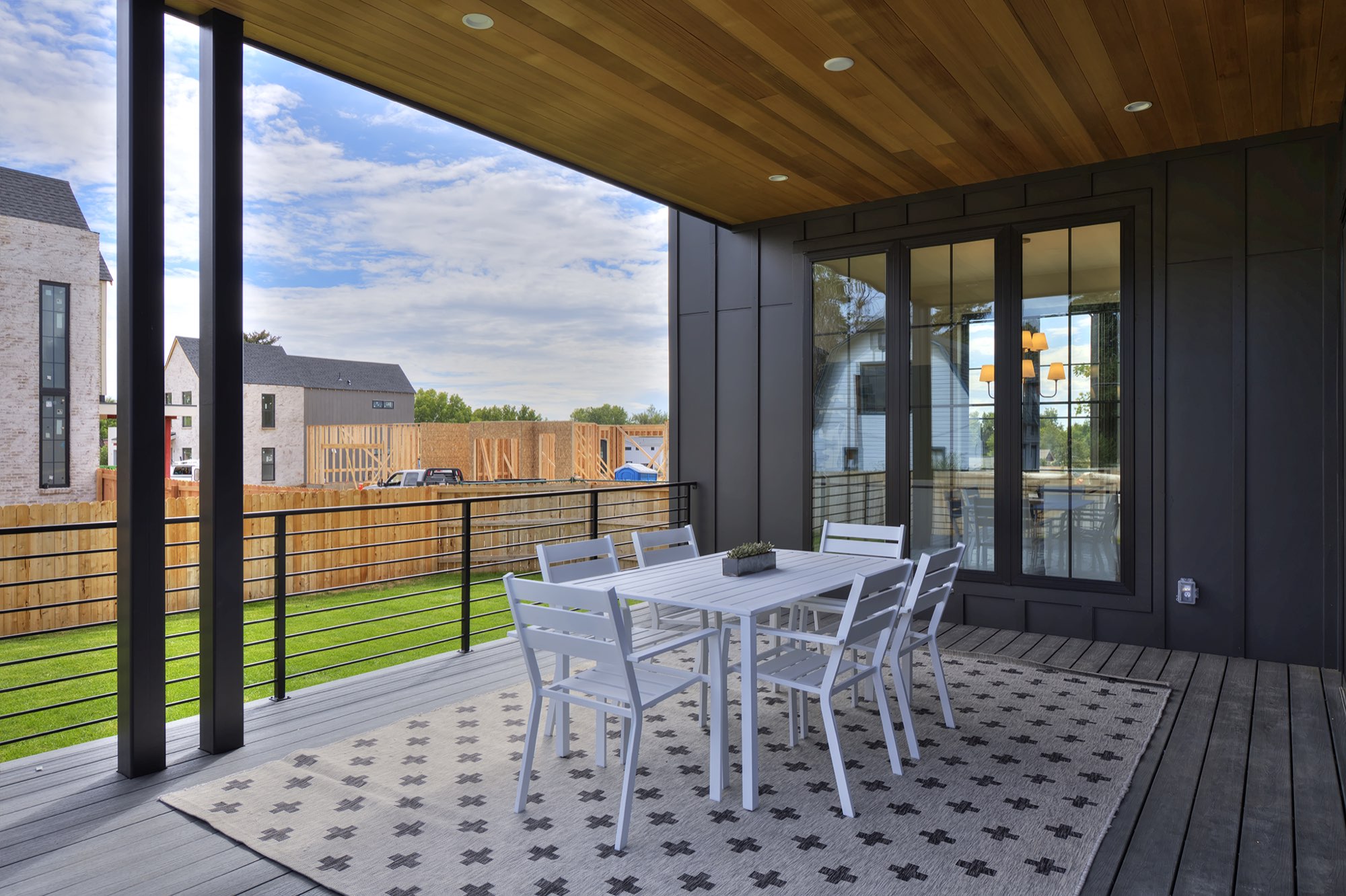 Covered deck with a wood-plank ceiling, recessed lights, black posts and a dining set beside the black-framed sliding doors
