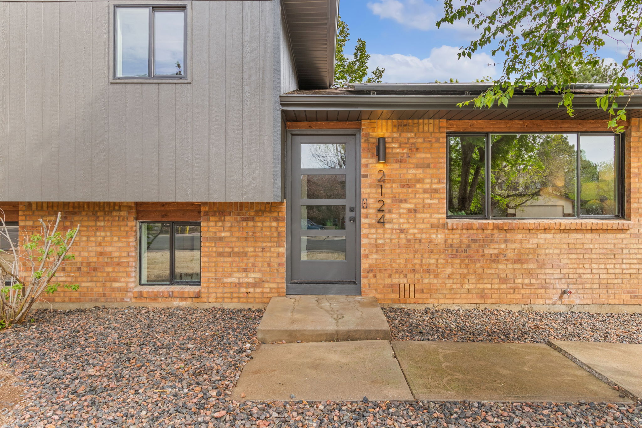 Entry with a modern glass-panel front door set between brick and gray siding
