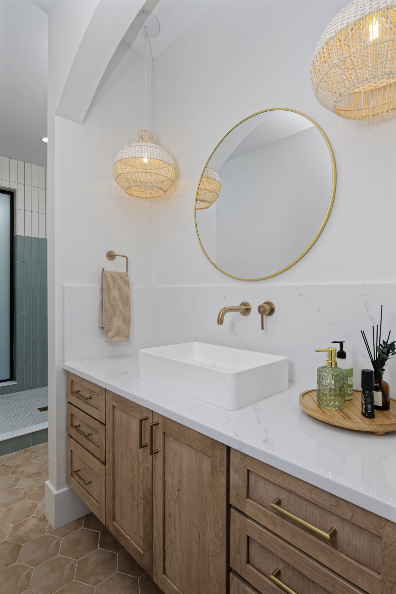 Second bathroom with a wood vanity, white vessel sink, round brass mirror, woven pendant and green tile shower