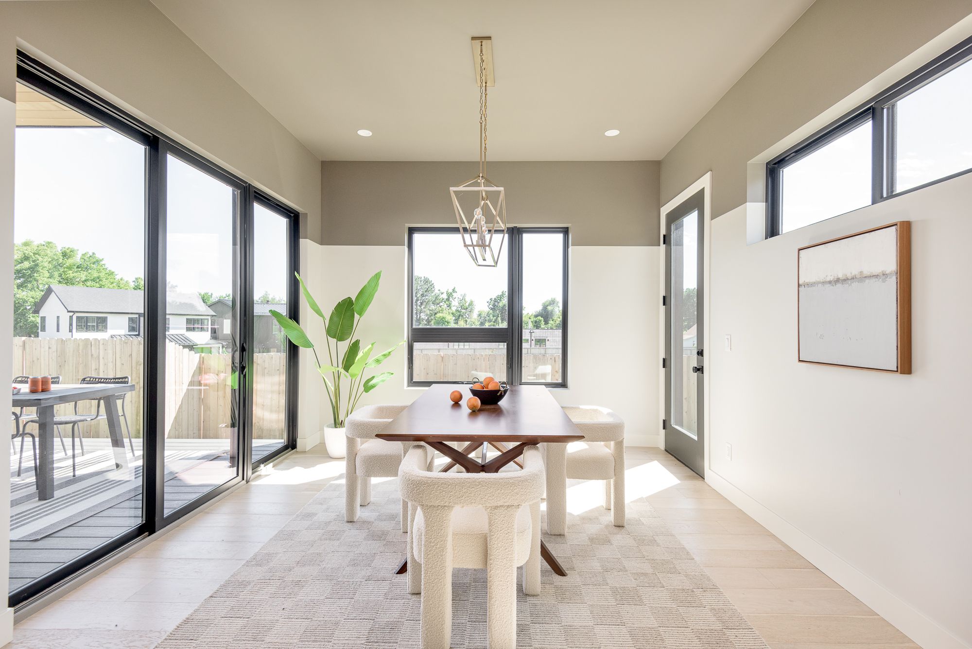 Dining table under a brass lantern chandelier with black sliders to the deck