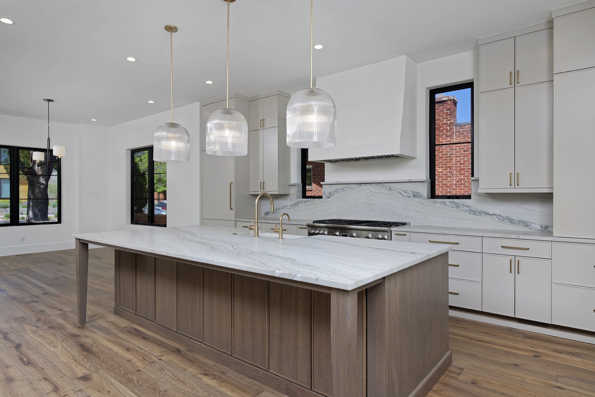 Kitchen from the side with the island, ribbed glass pendants, white hood and stone backsplash