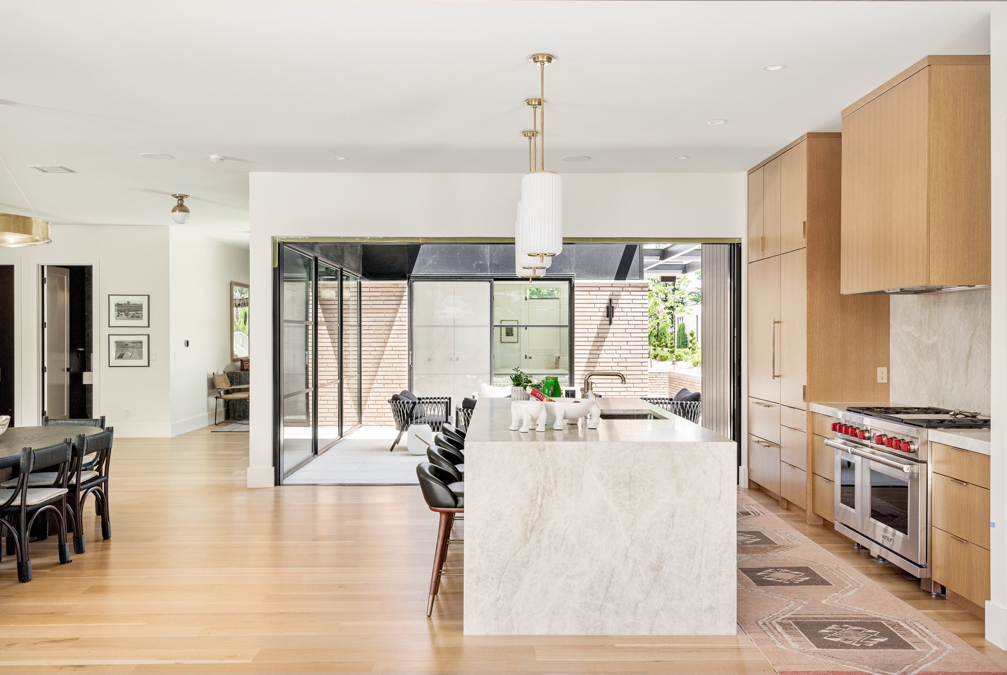 Wide kitchen with a stone waterfall island, light wood cabinets, a range and black-framed doors open to the patio