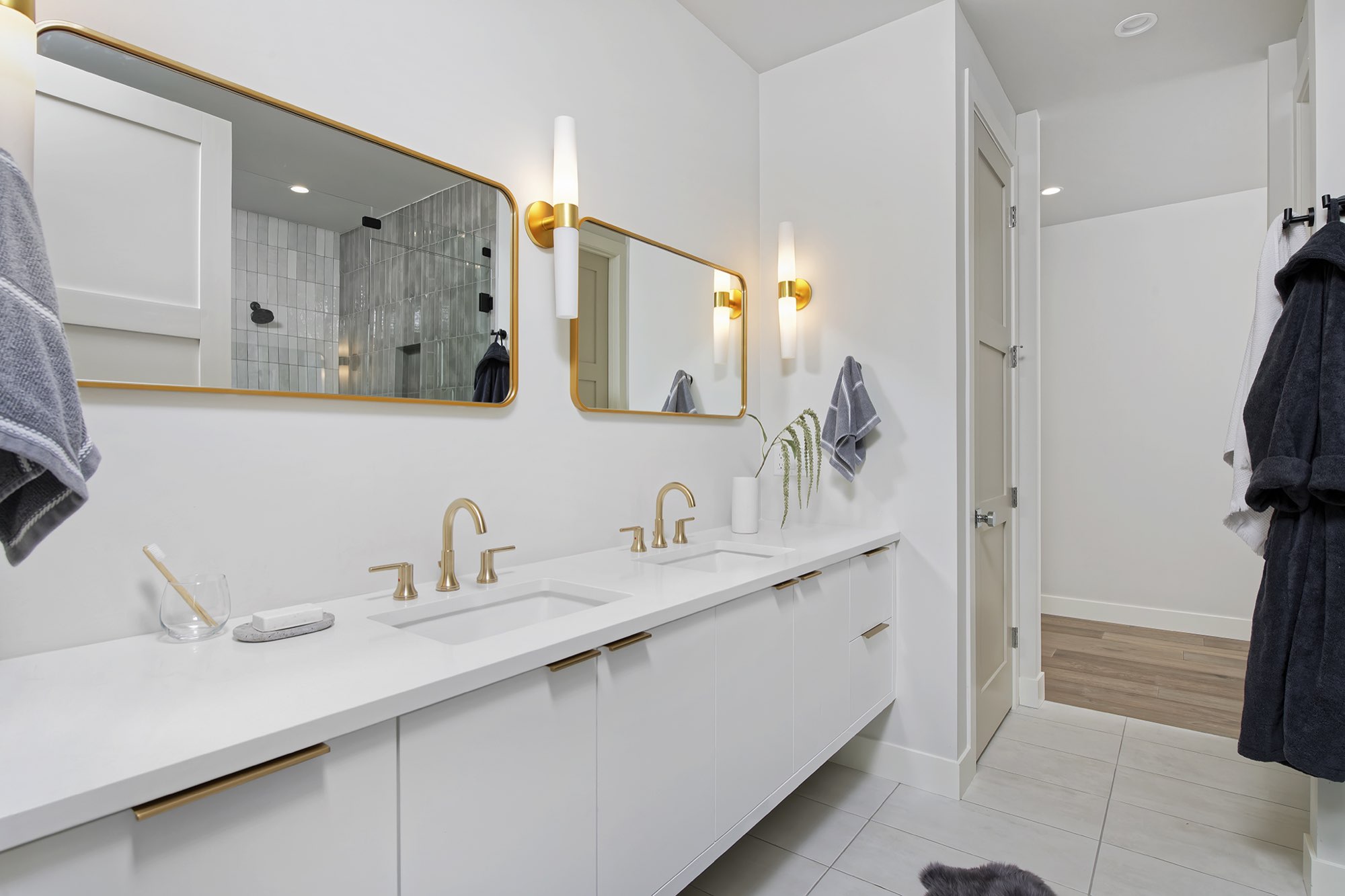 Primary bath with a long white double vanity, gold-framed mirrors, tall sconces and a door to the bedroom