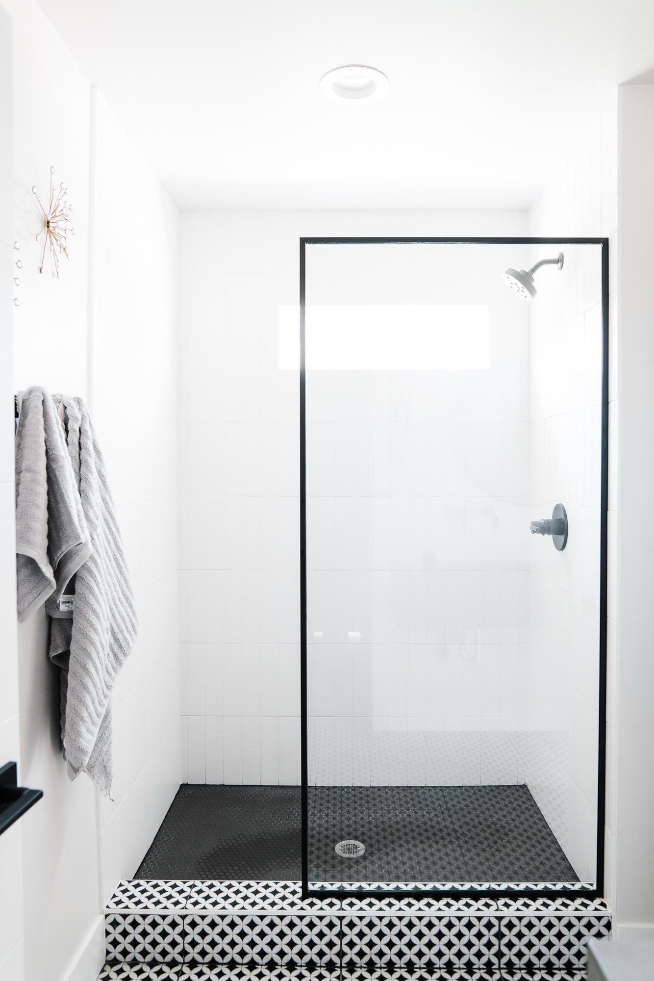 Walk-in shower with a black-framed glass panel and a black and white patterned tile floor
