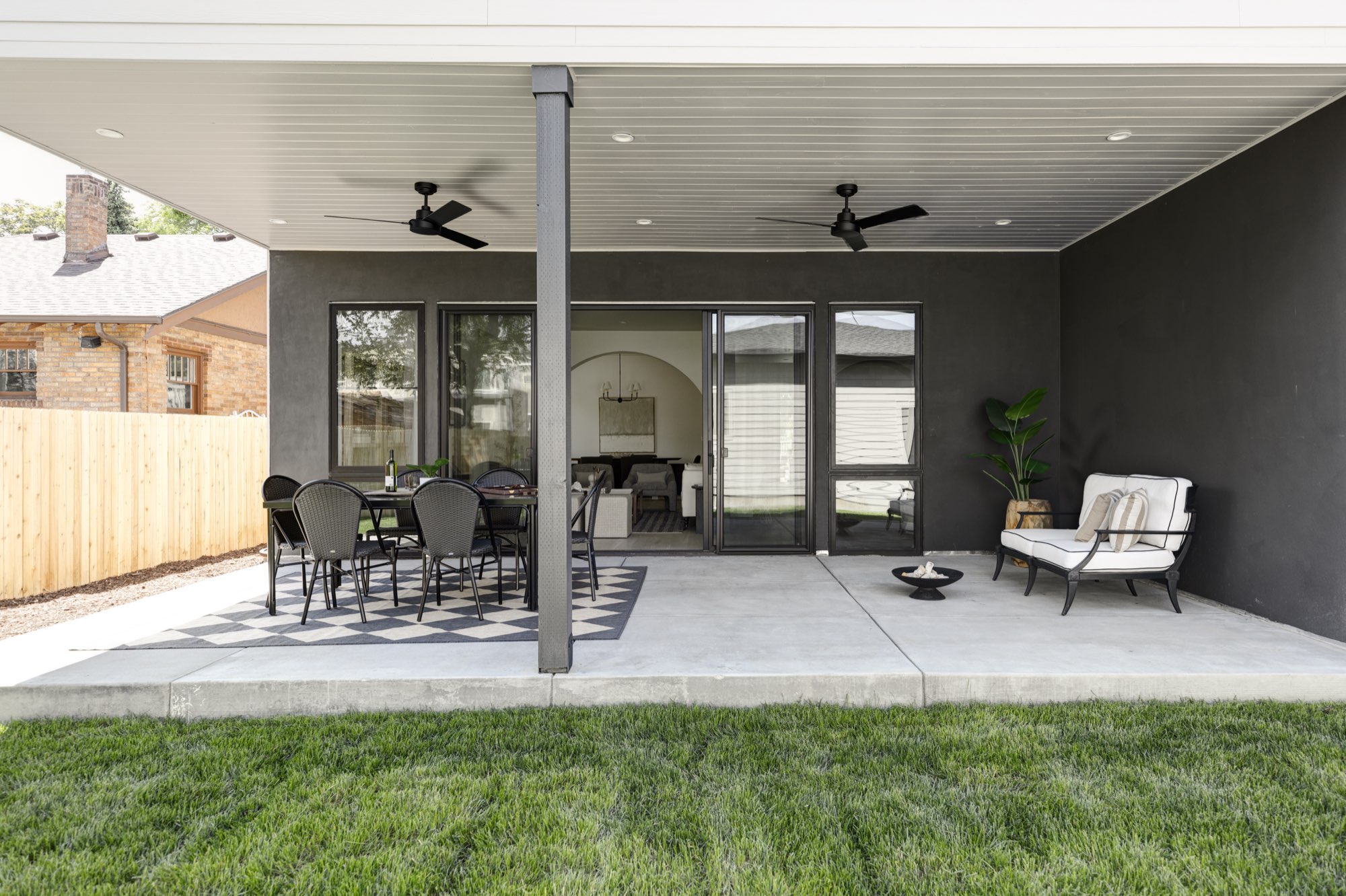 Covered back patio with a concrete floor, two ceiling fans, black-framed sliding doors and a dark stucco wall