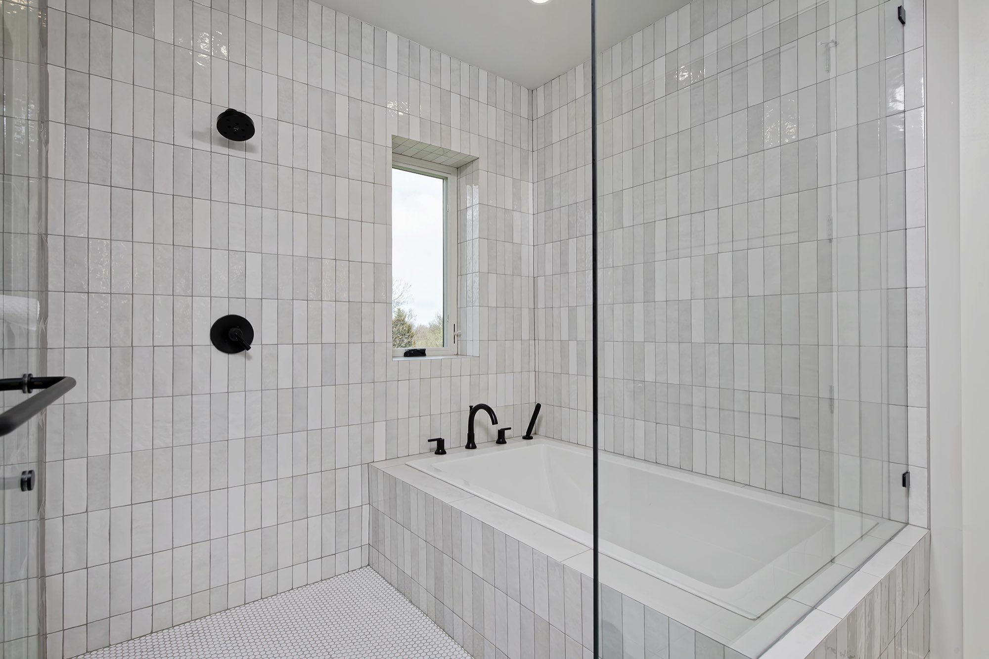 Glass-enclosed shower and tiled tub in glossy vertical tile with black fixtures and a small window