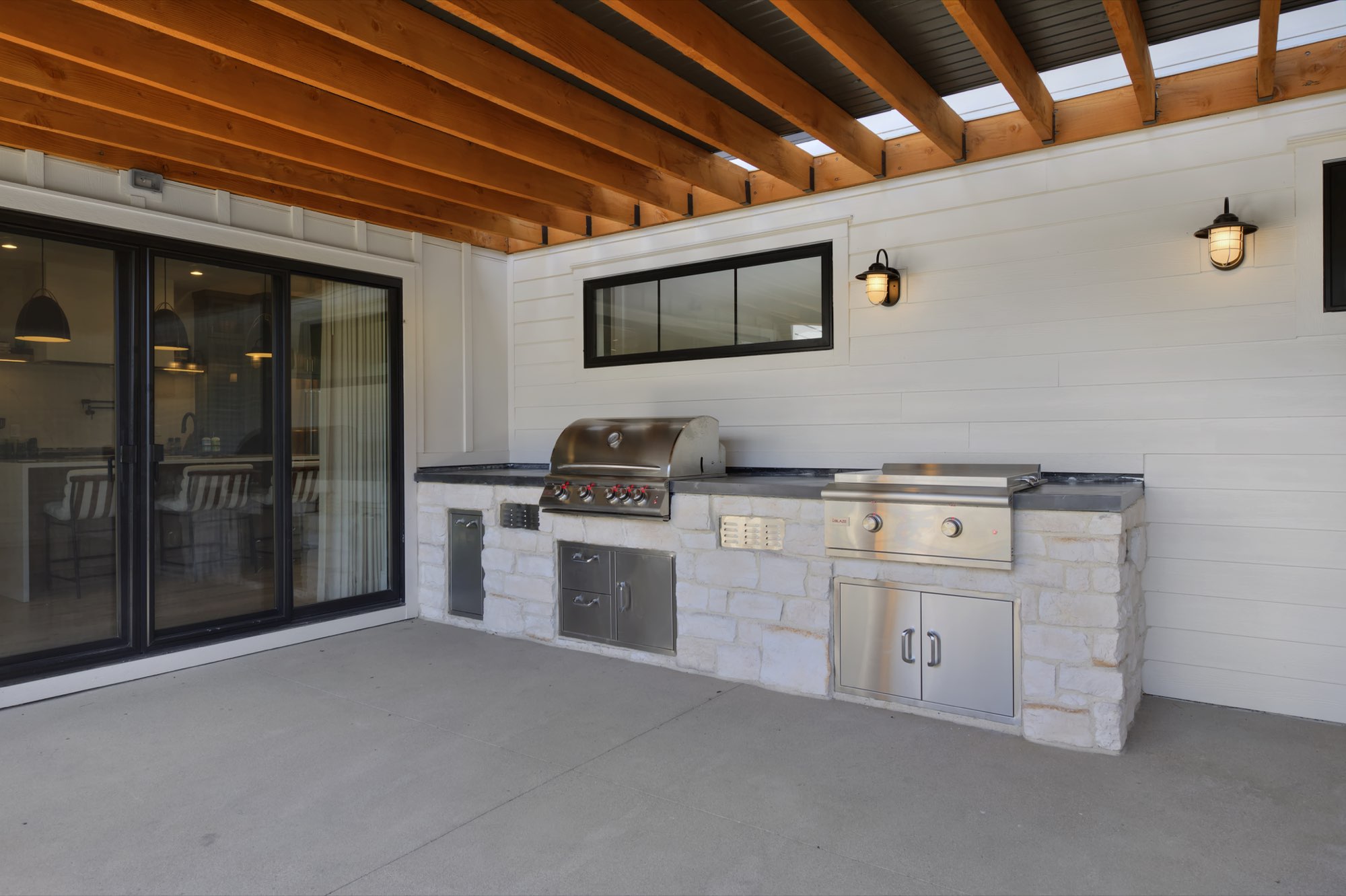 Outdoor kitchen with a built-in grill and cabinets faced in light stone under timber rafters