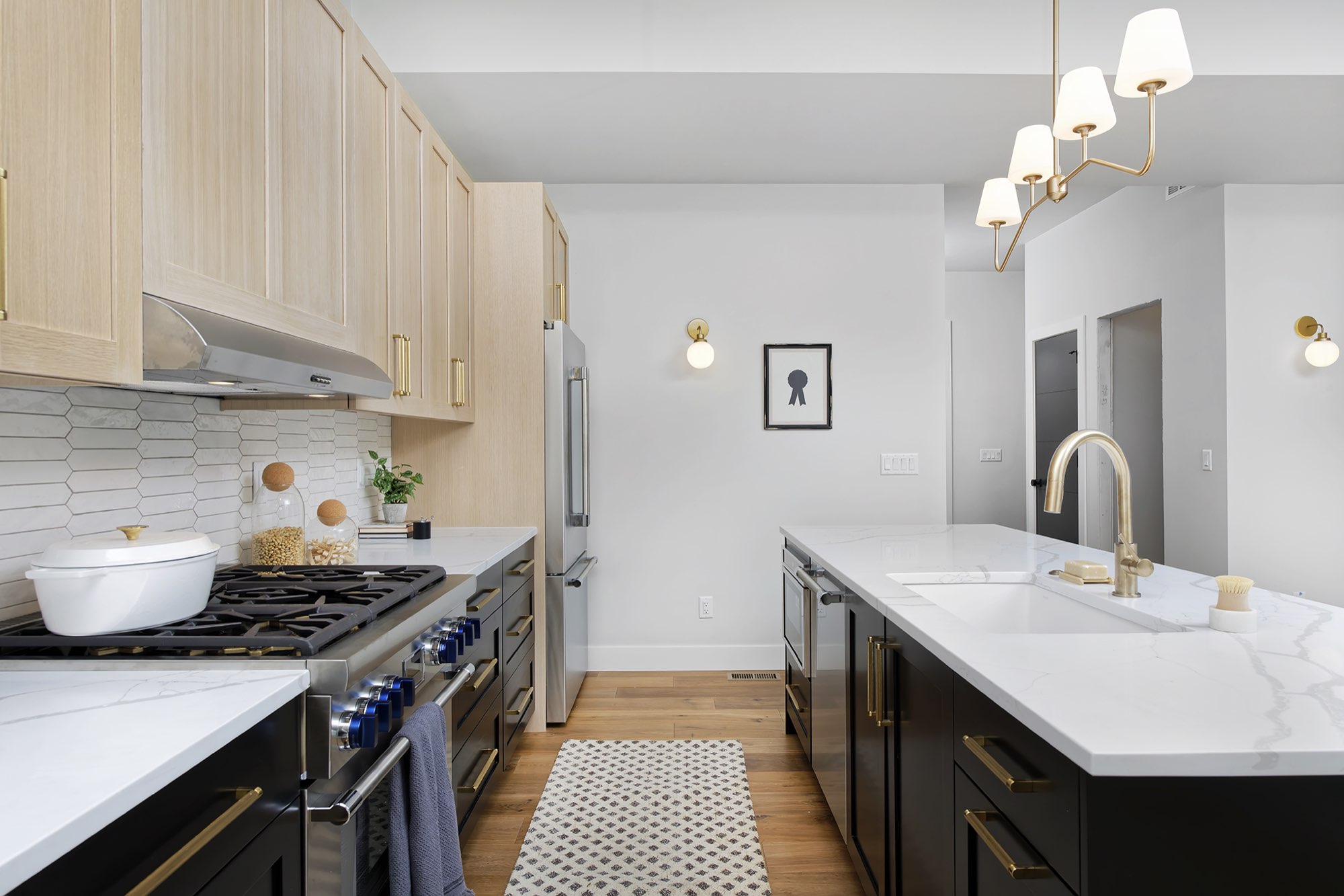 Range with a stainless hood and white tile backsplash beside the black island and brass faucet