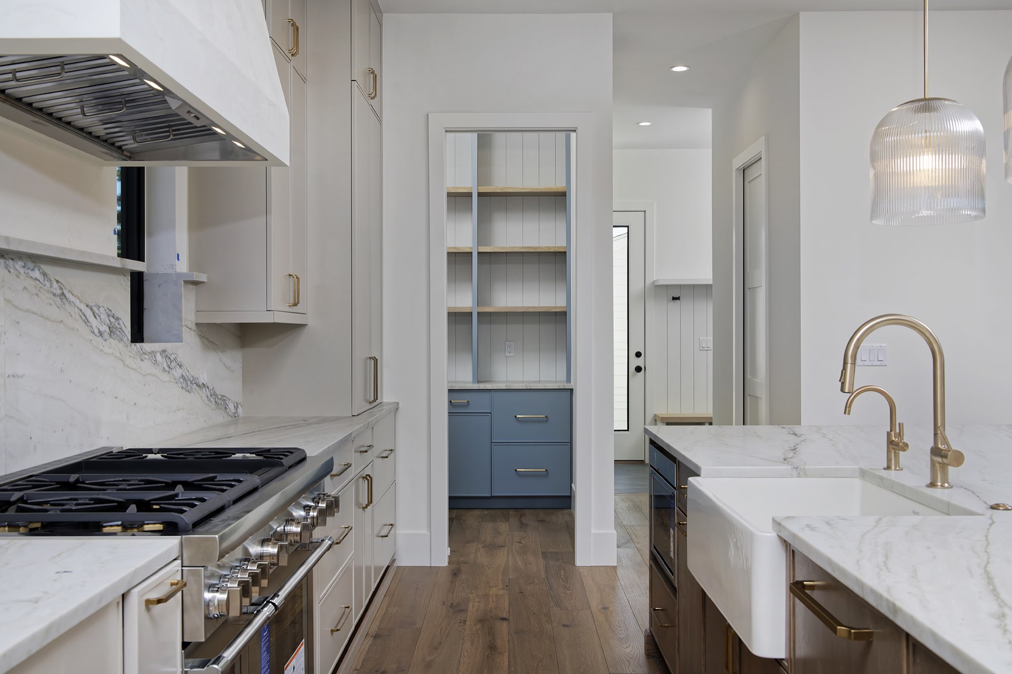 Kitchen with a farmhouse sink, brass faucet, gas range and a blue built-in seen through the doorway