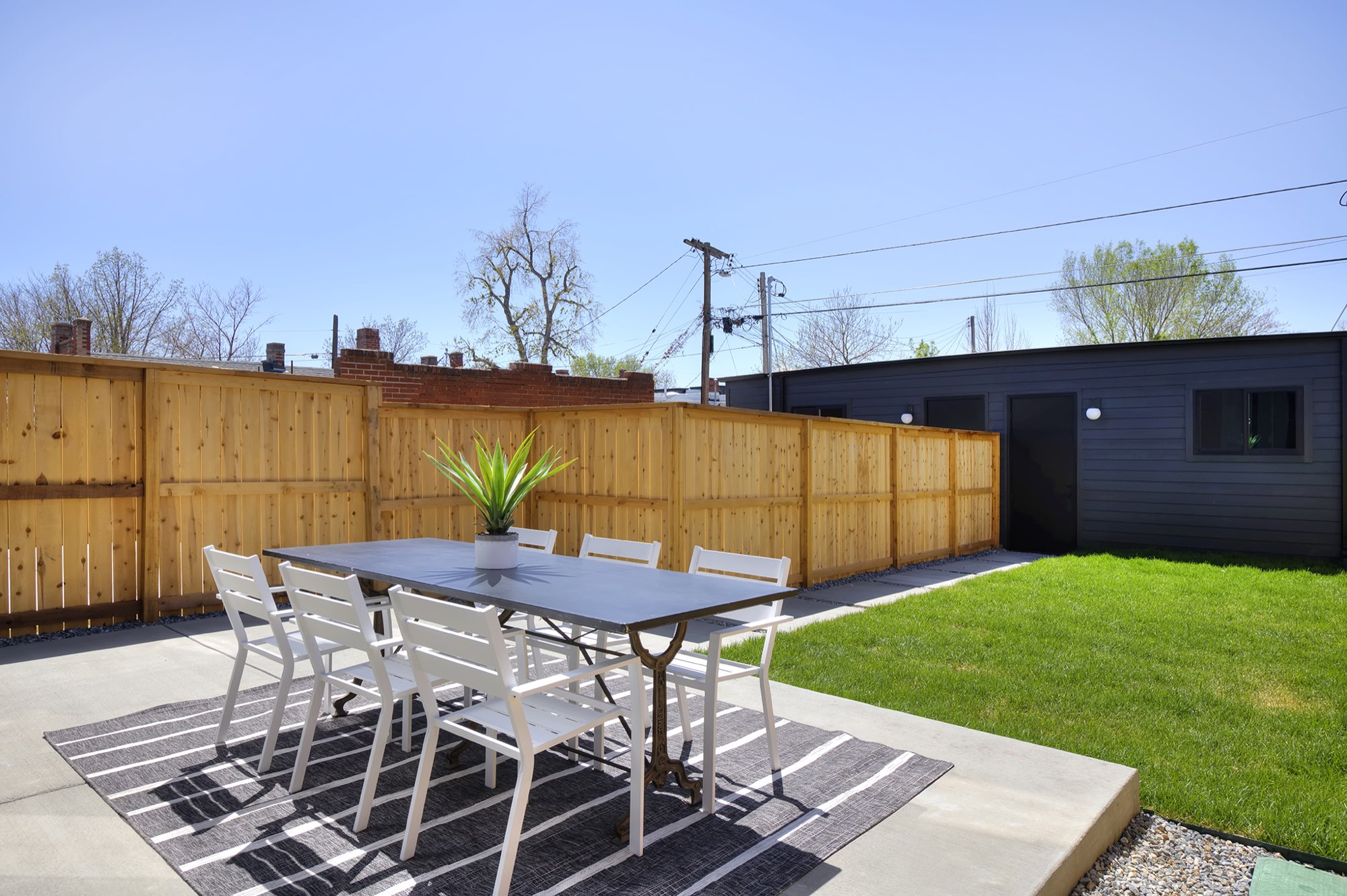 Concrete patio with a dining table and rug beside a lawn and a wood privacy fence