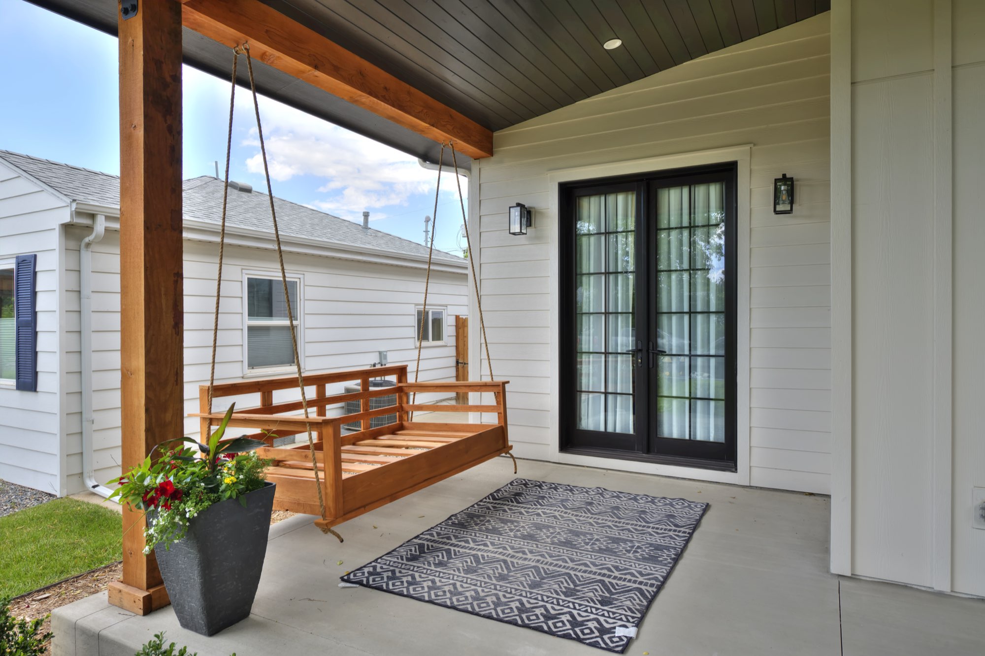 Porch swing and black-framed French doors under the porch ceiling with recessed lights