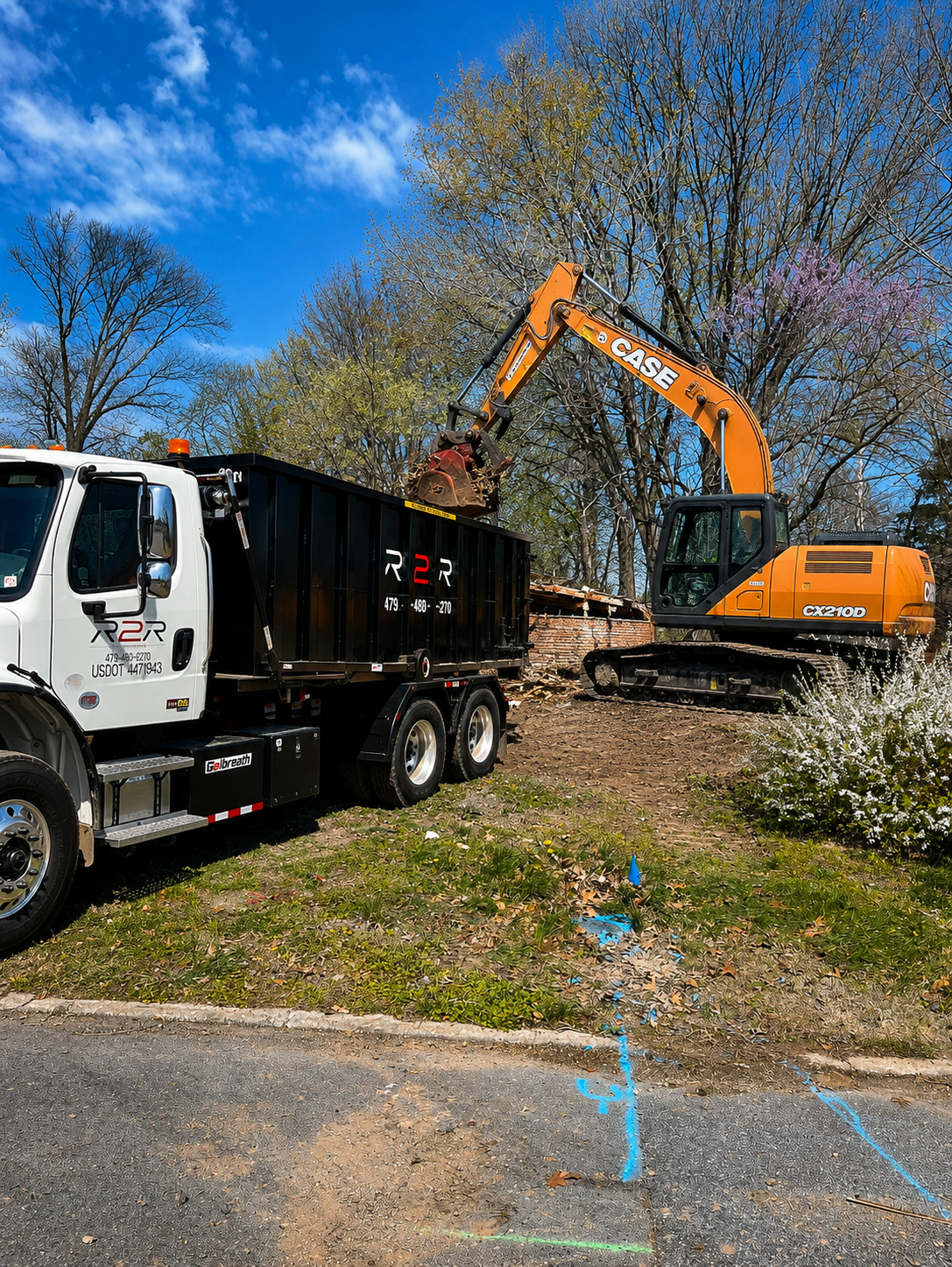 Excavator loading demolition debris into an R2R roll-off dumpster on the truck