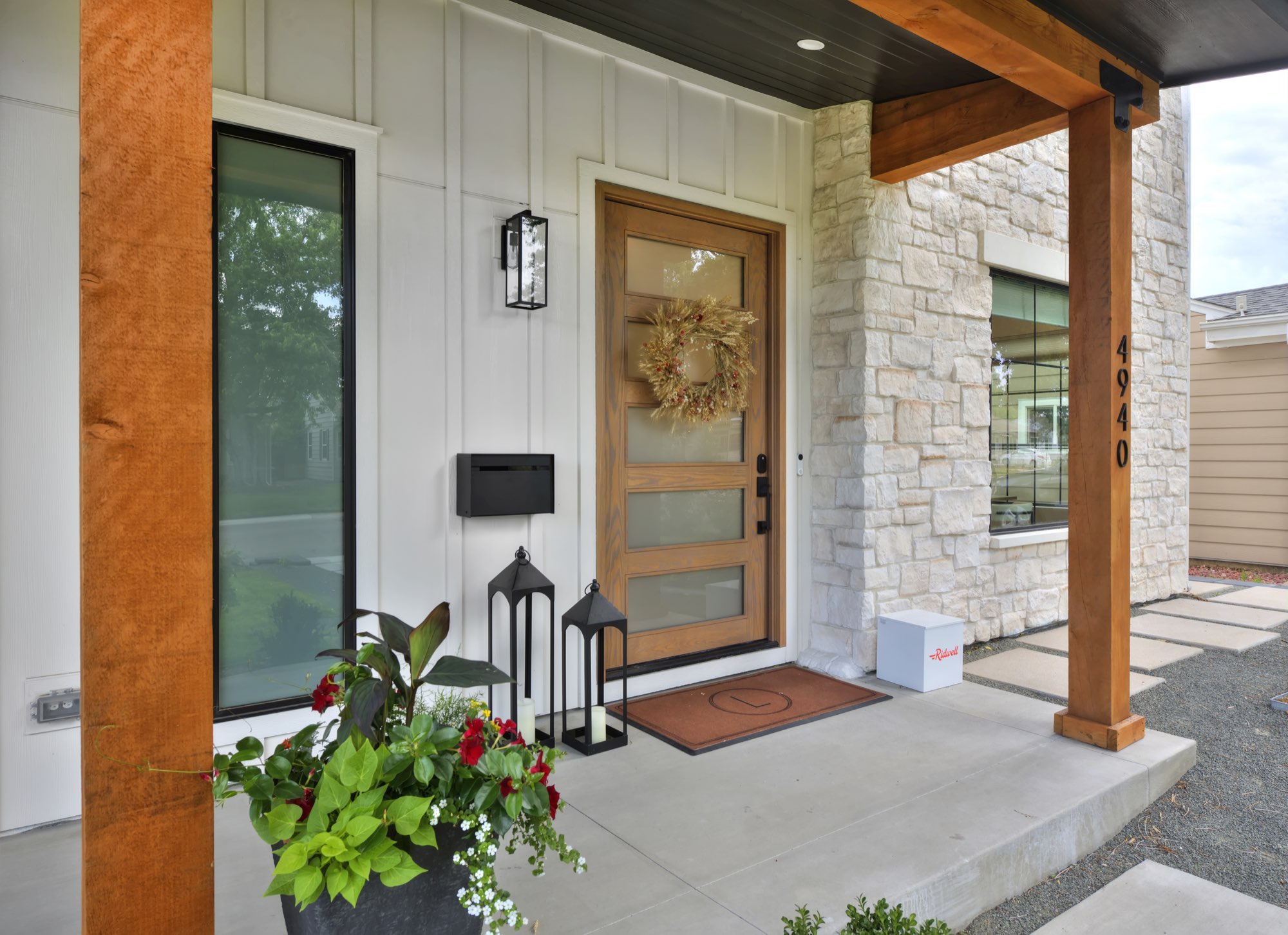 Wood front door with frosted glass panels, a wreath and the house number beside light stone and board-and-batten siding