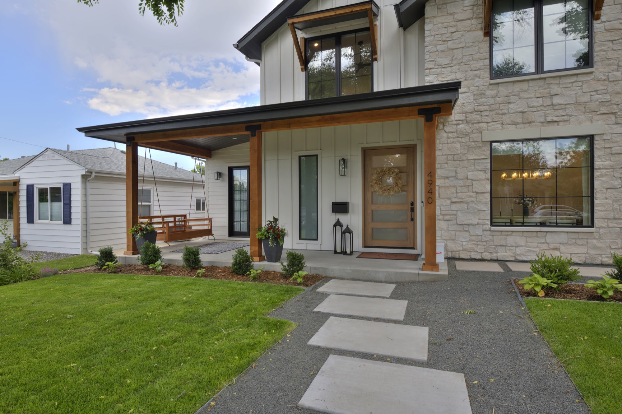 Front of the Denver custom home with white board-and-batten siding, light stone, a timber-post porch and concrete steppers across the lawn
