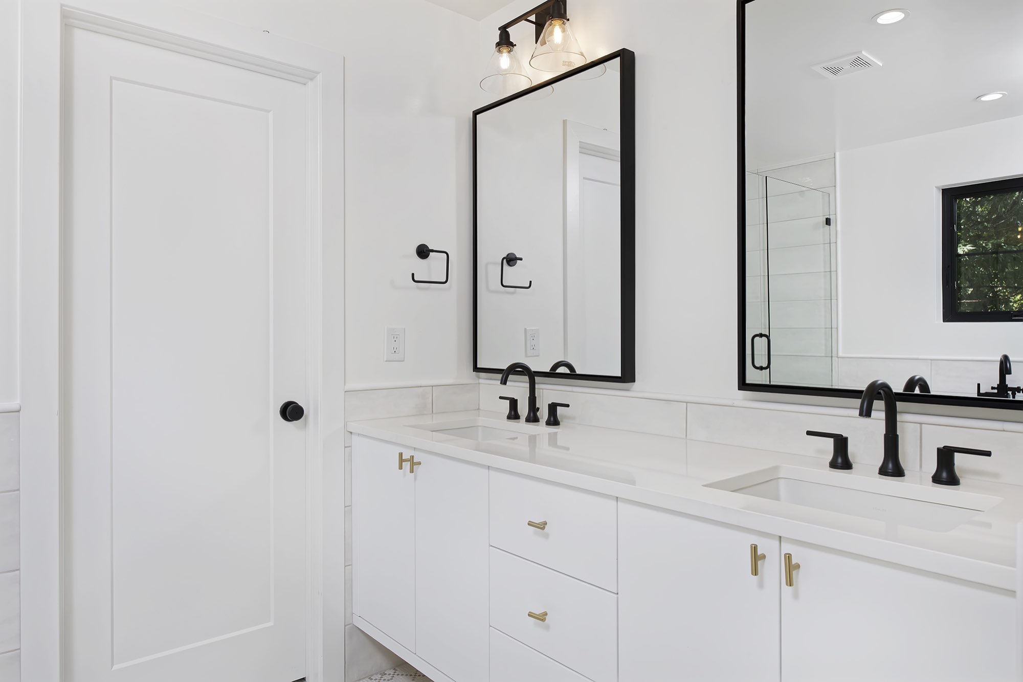 Double white vanity with black faucets, black-framed mirrors and a mirror reflecting the shower