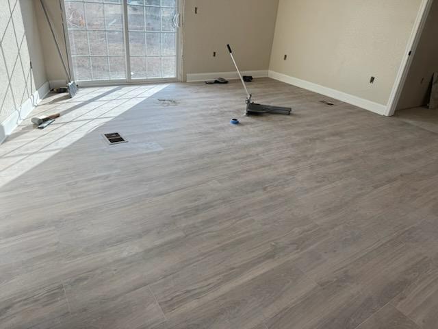 Light grey luxury vinyl plank being installed across a mobile home room with a pull bar in use