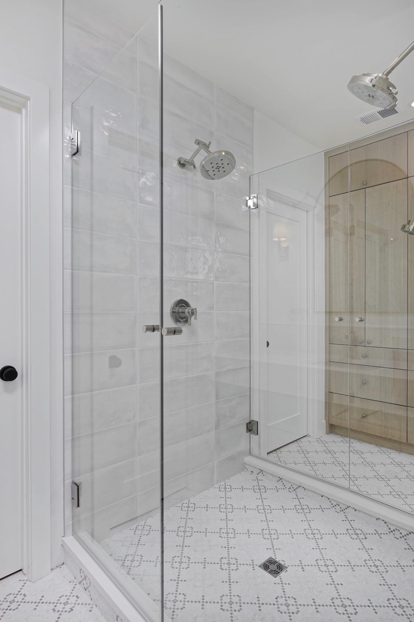 Frameless glass shower in glossy white tile with a patterned mosaic floor