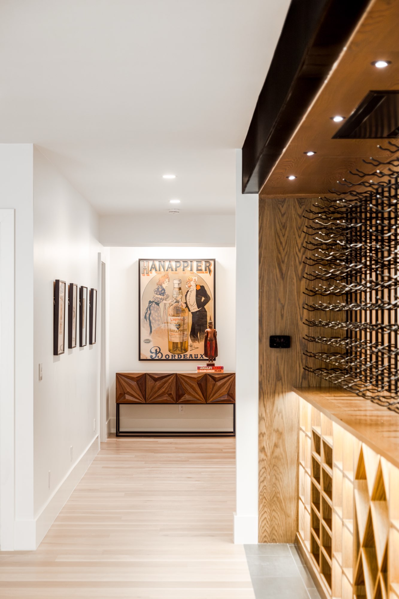 Hallway with light wood floors beside the wine wall, with lit wood cubbies and racks