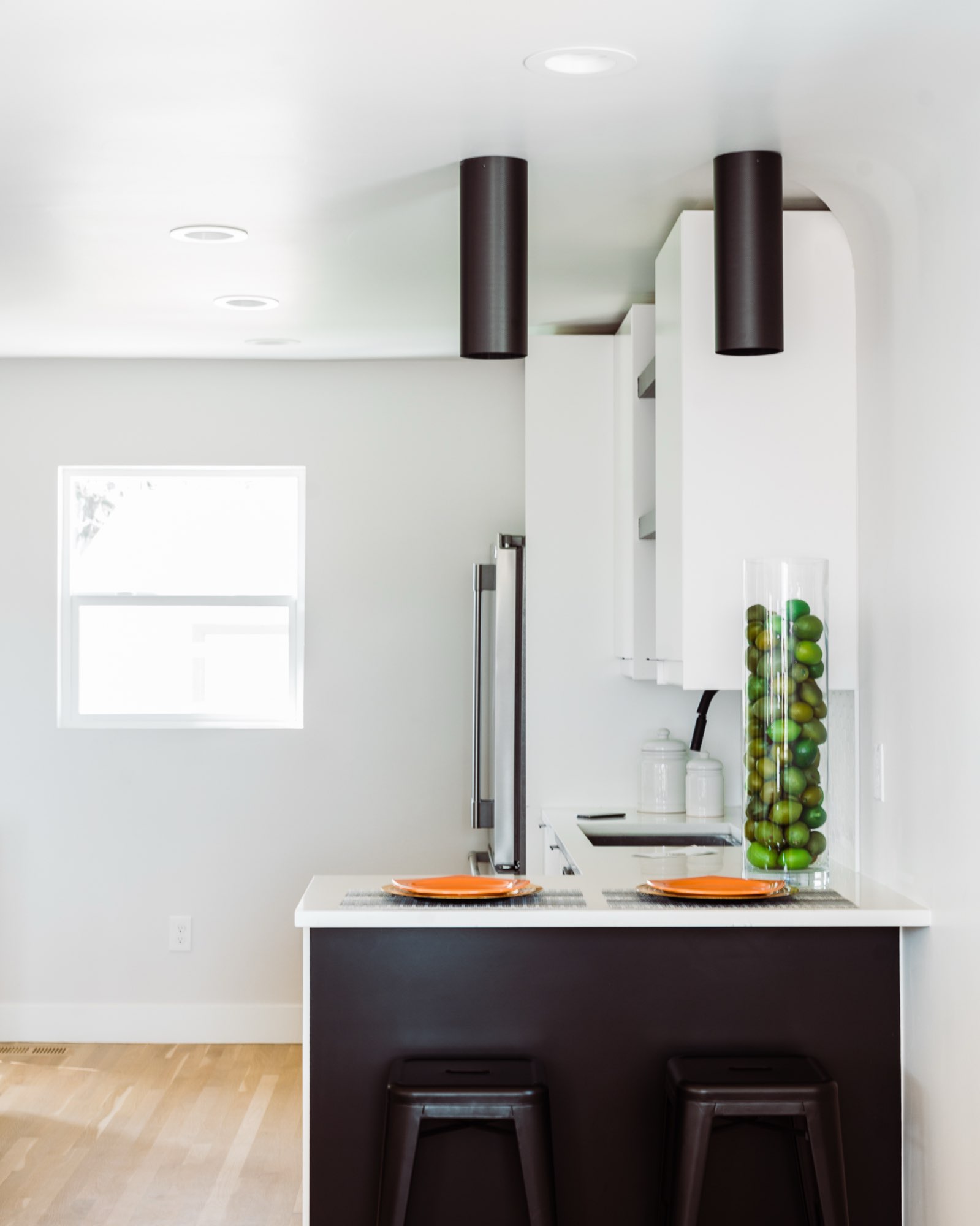 Kitchen peninsula with black front panels, black stools, white counters and a tall glass vase of limes