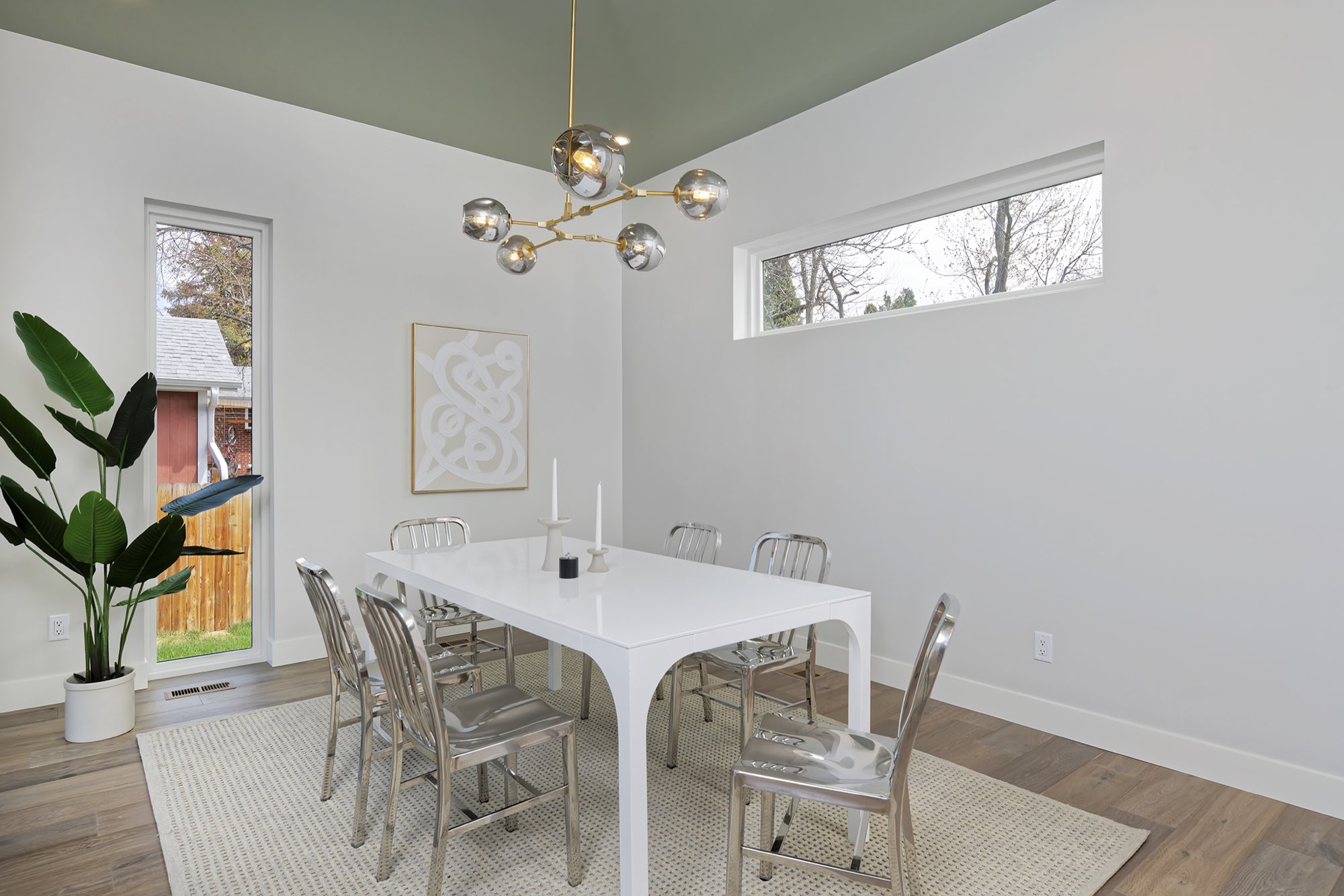 Dining room with tall windows and doors toward the deck, a plant and a white table