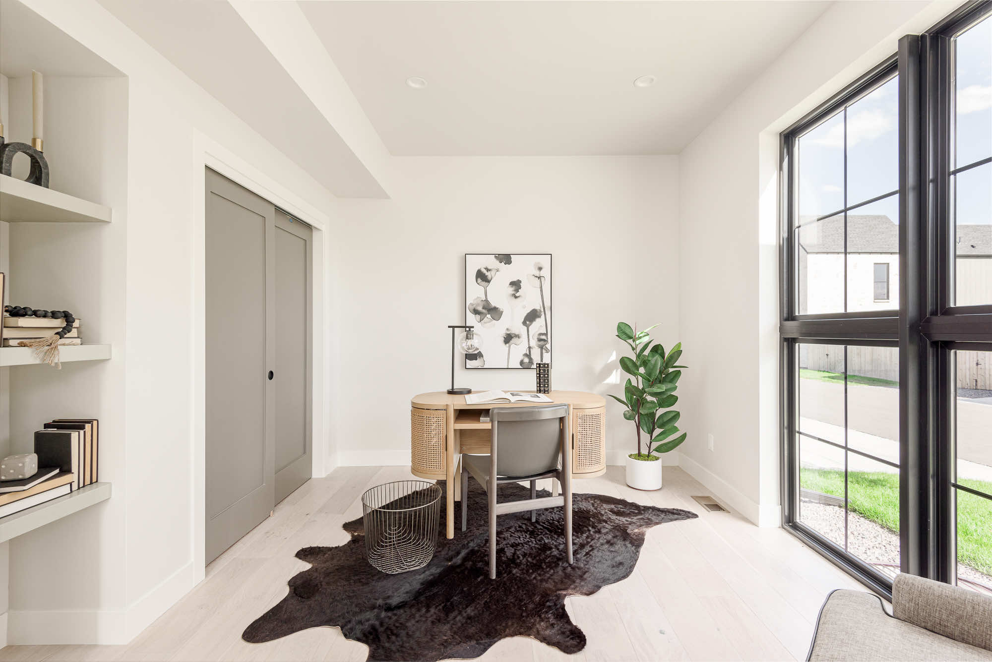 Front office with a wood desk, tall black-framed corner windows and built-in shelves