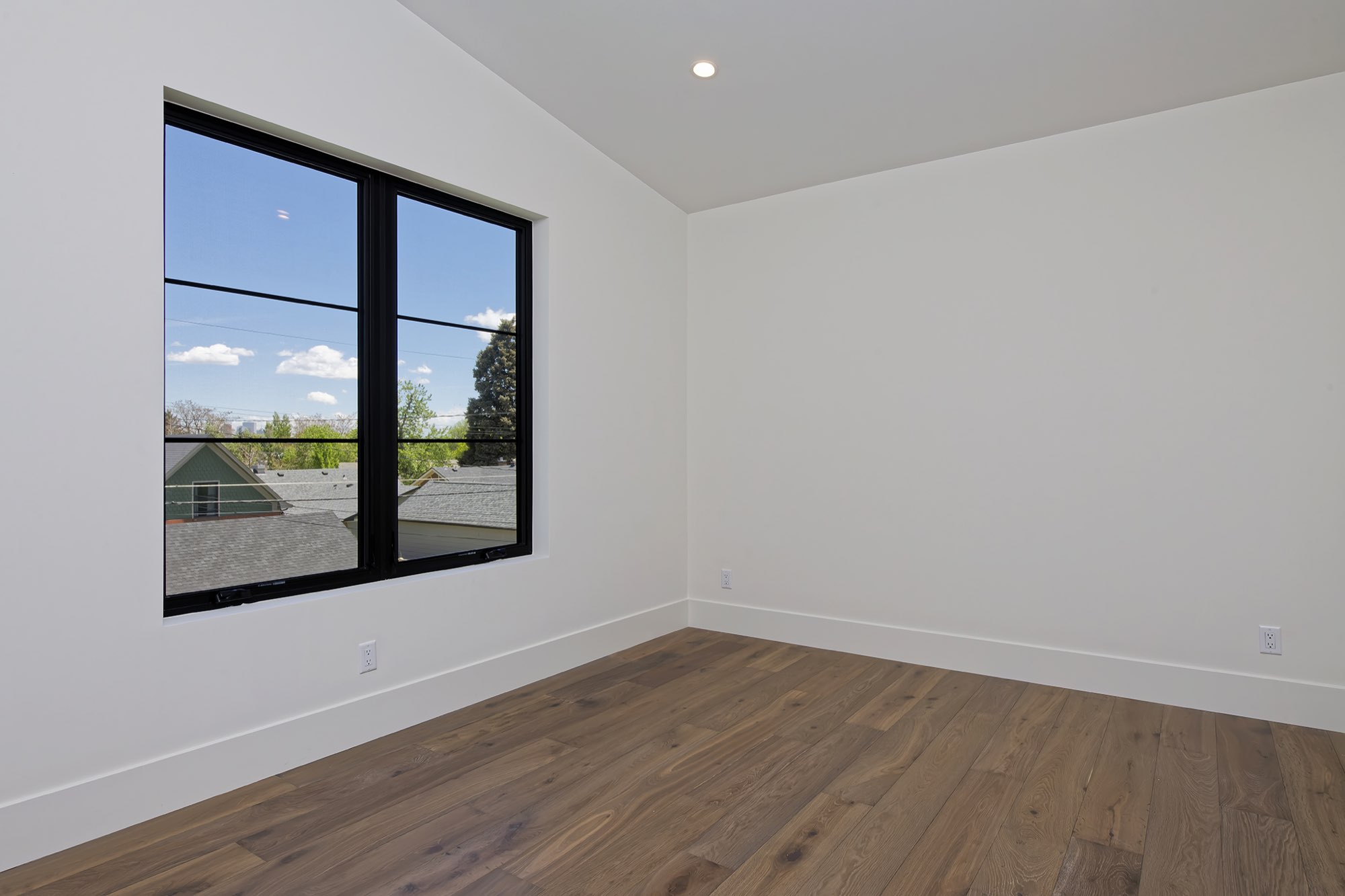 Upstairs bedroom with a vaulted ceiling, wood floors and a large black-framed window