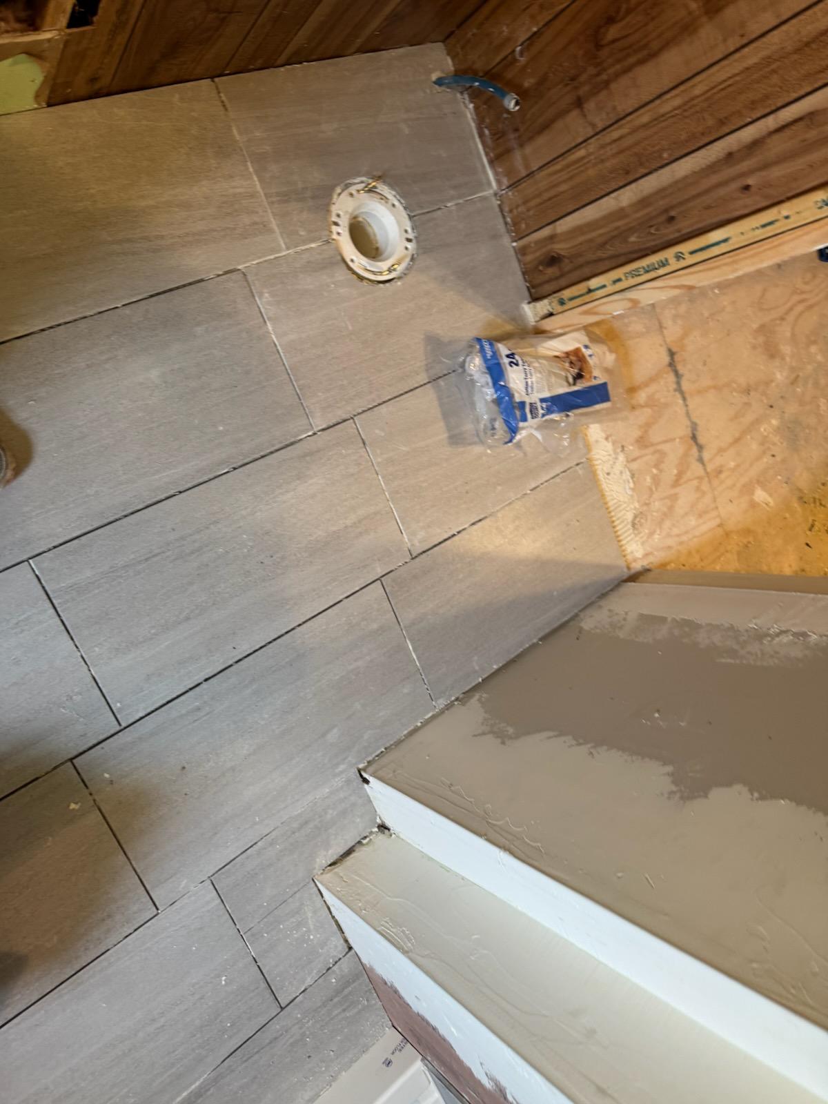 Grey vinyl tile being set in a mobile home bathroom around a toilet flange with the repaired subfloor still visible at the edge