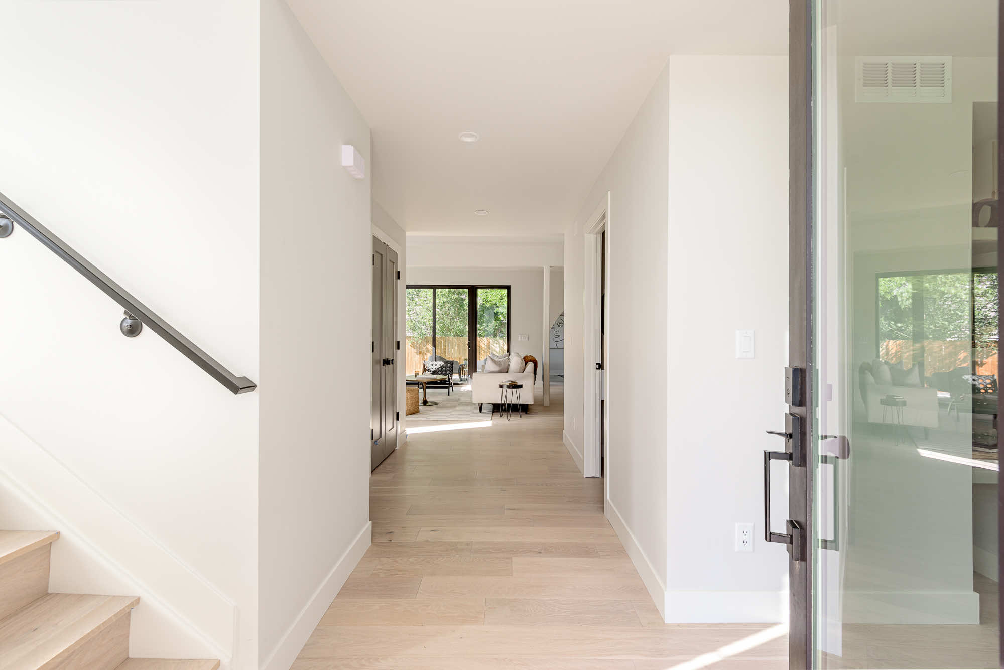 Entry hall from the front door with light wood floors, a black stair rail and the living room at the far end