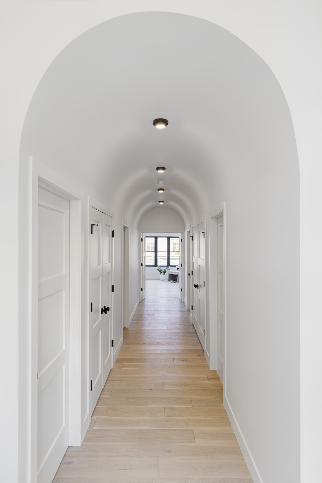 Arched barrel-vault hallway with recessed lights, white paneled doors and light wood floors