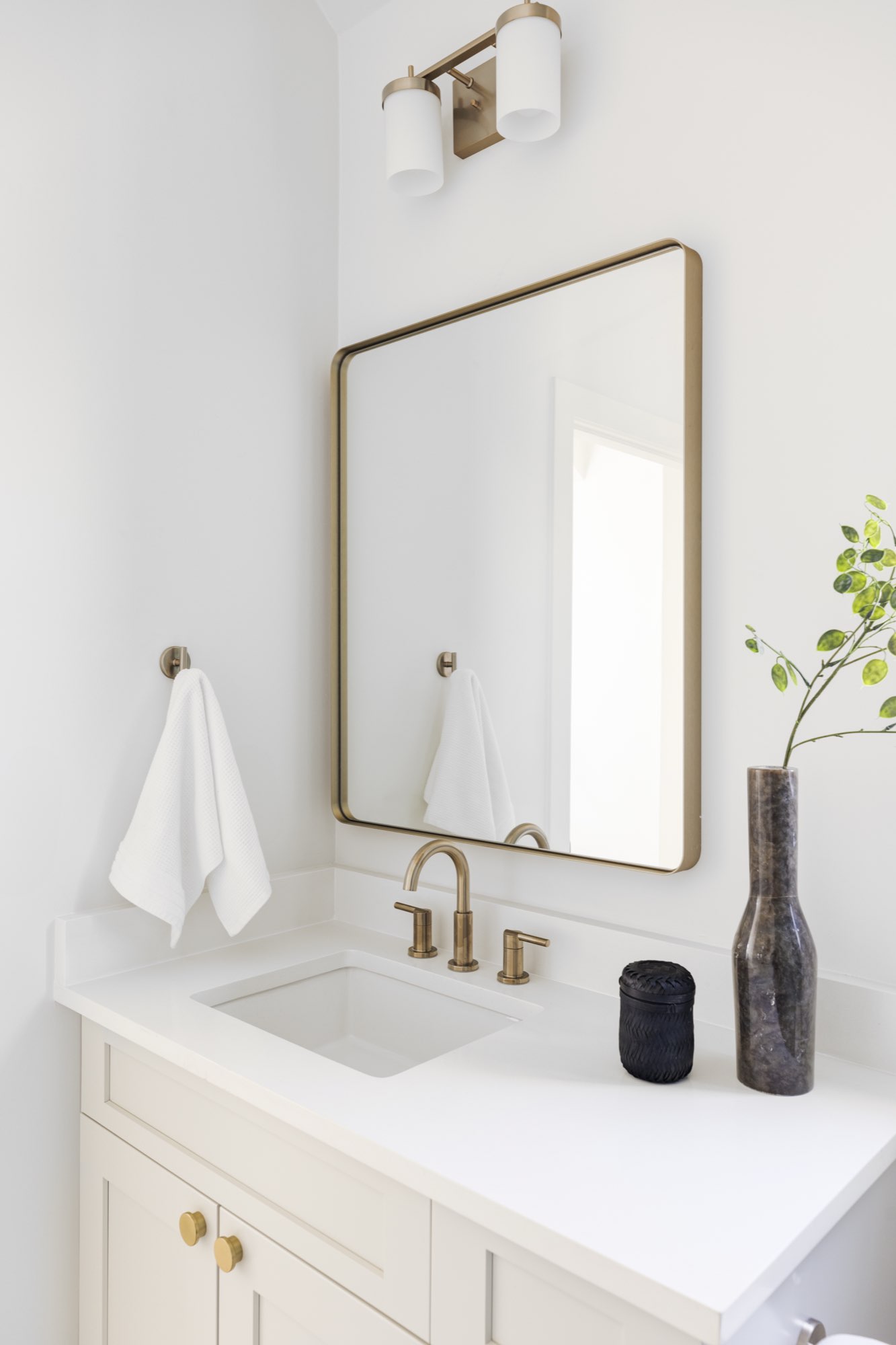Powder room with a brass-framed mirror, brass faucet and a white vanity with brass knobs