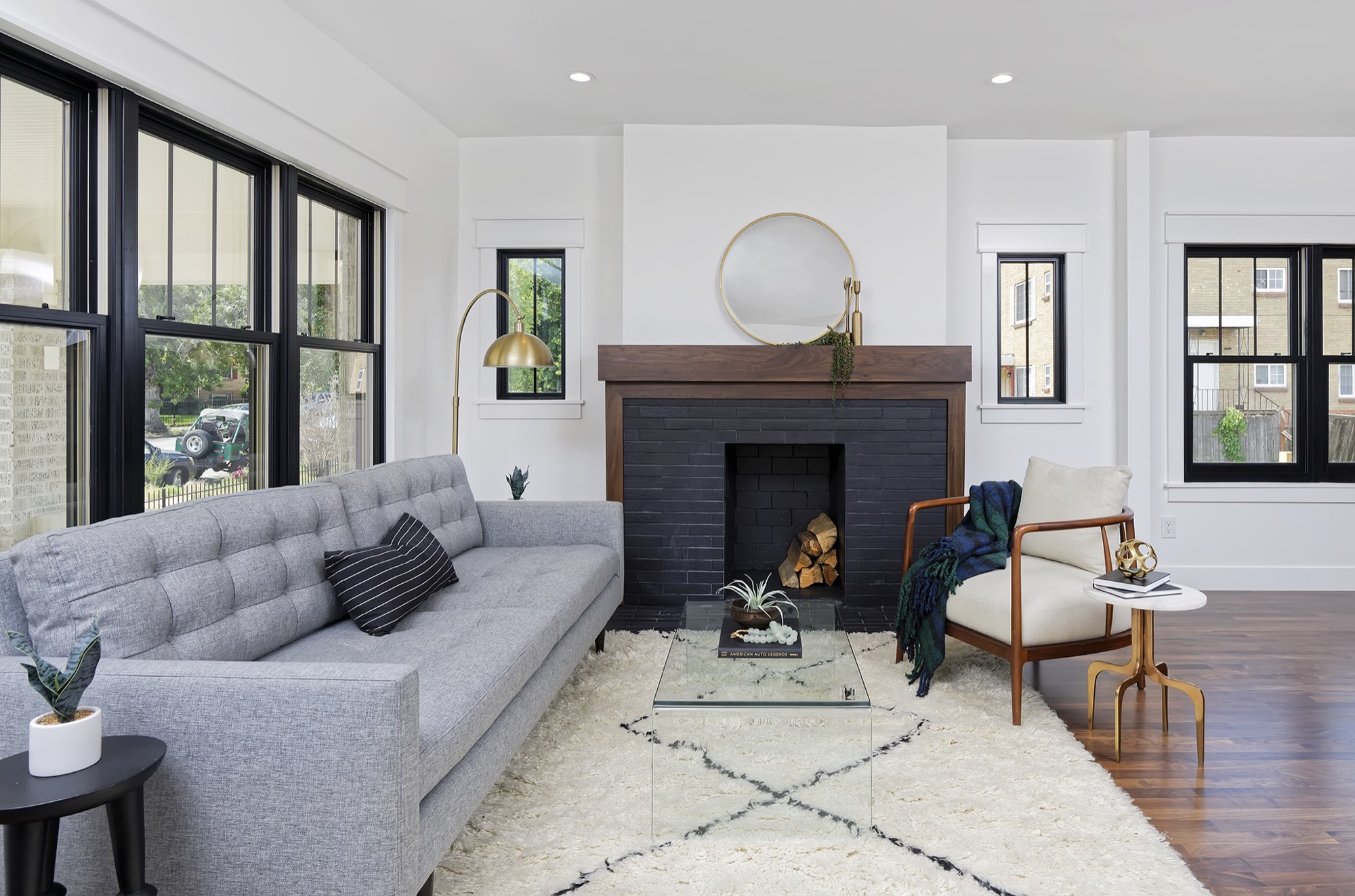Dark brick fireplace with a wood mantel and round mirror beside tall black-framed windows