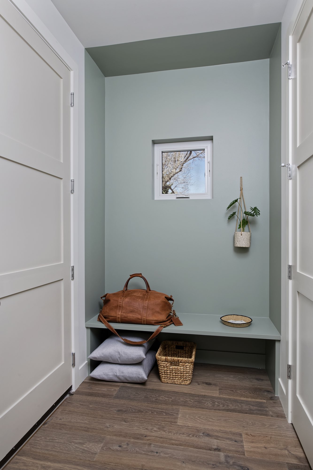 Mudroom niche in sage green with a built-in bench, a small window and wood floors