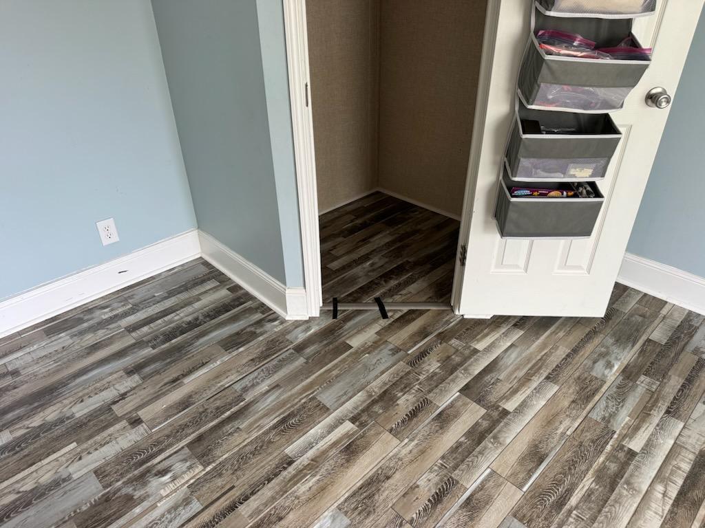 Two plank flooring finishes meeting at a mobile home doorway, weathered grey into dark brown