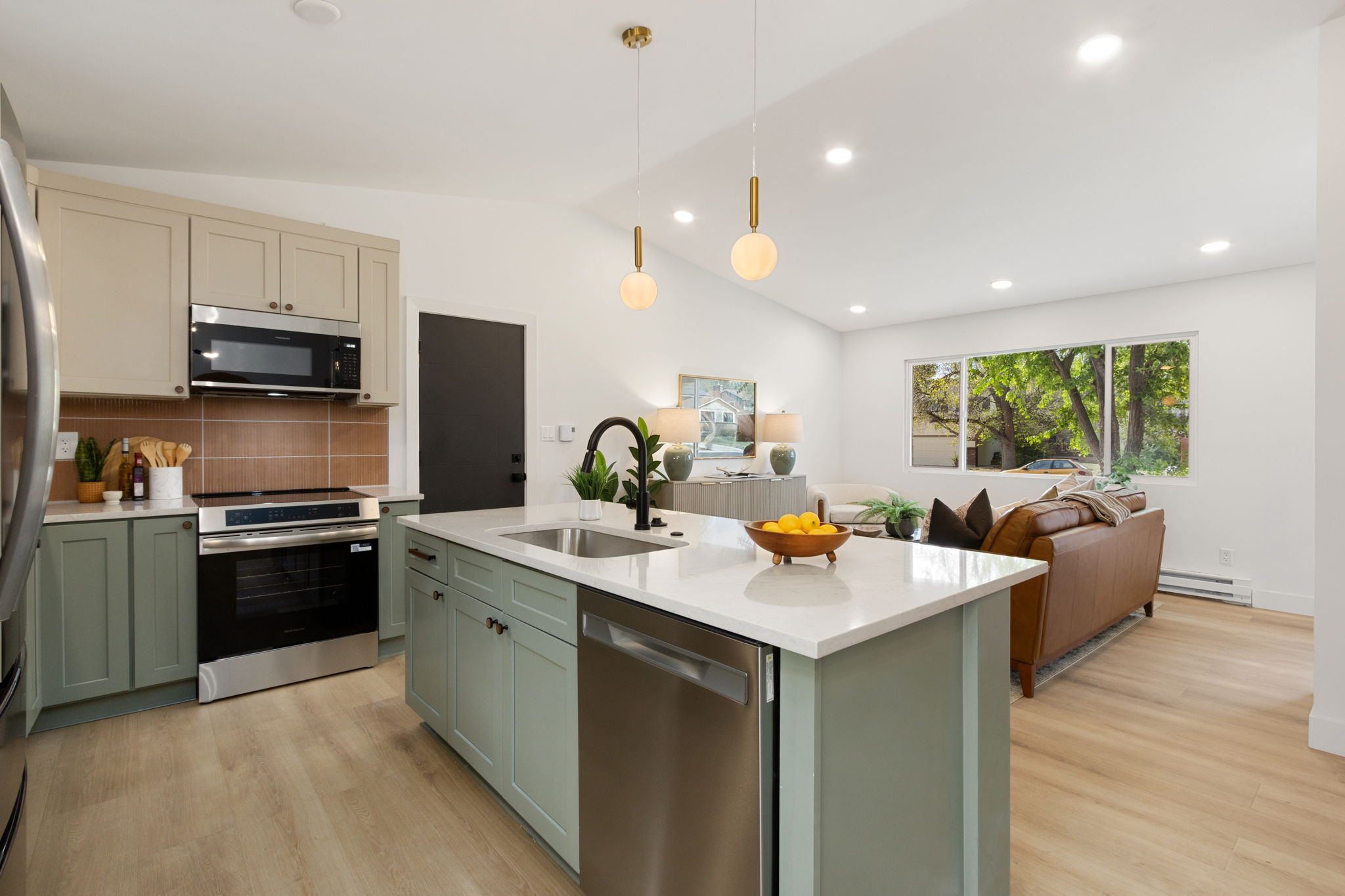 Kitchen with a sage-green island, cream upper cabinets, white quartz counters and a terracotta-tone tile backsplash behind the range