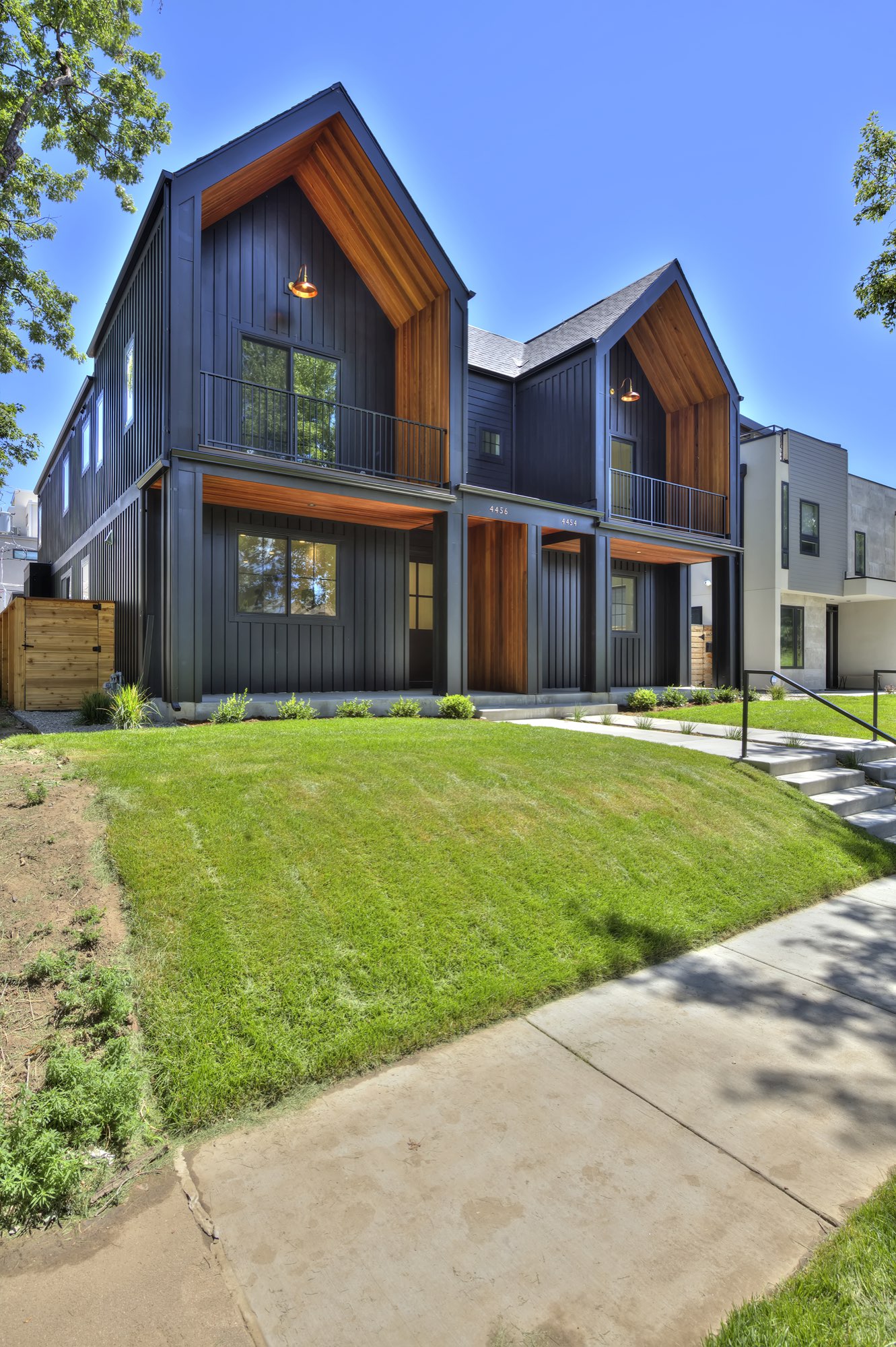Straight-on view of the duplex porches with wood-toned ceilings, black vertical siding, black columns and concrete steps up the lawn