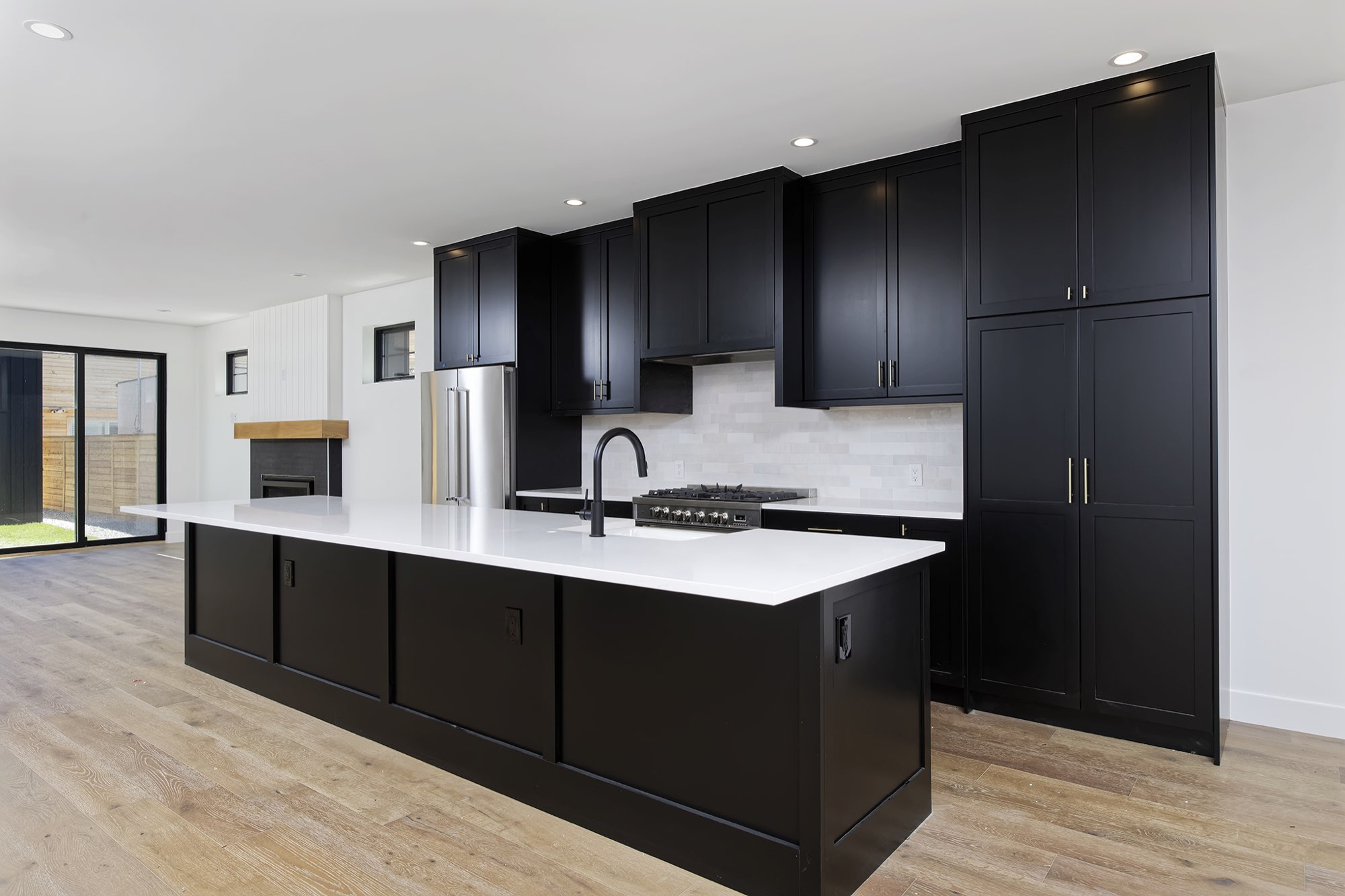 Kitchen with a tall black pantry wall, long island and a fireplace beyond