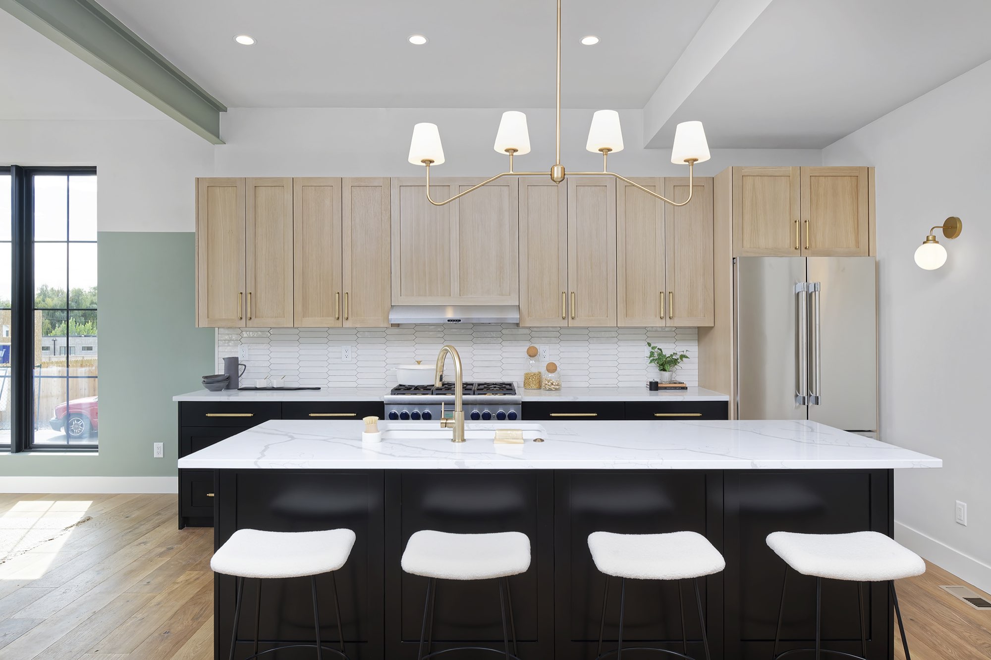 Straight-on view of the black island with four white stools, light wood cabinets and a stainless refrigerator