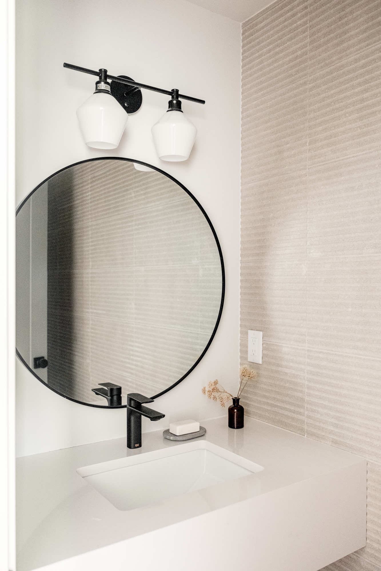 Powder room with a round black mirror, a floating white sink and ribbed accent tile