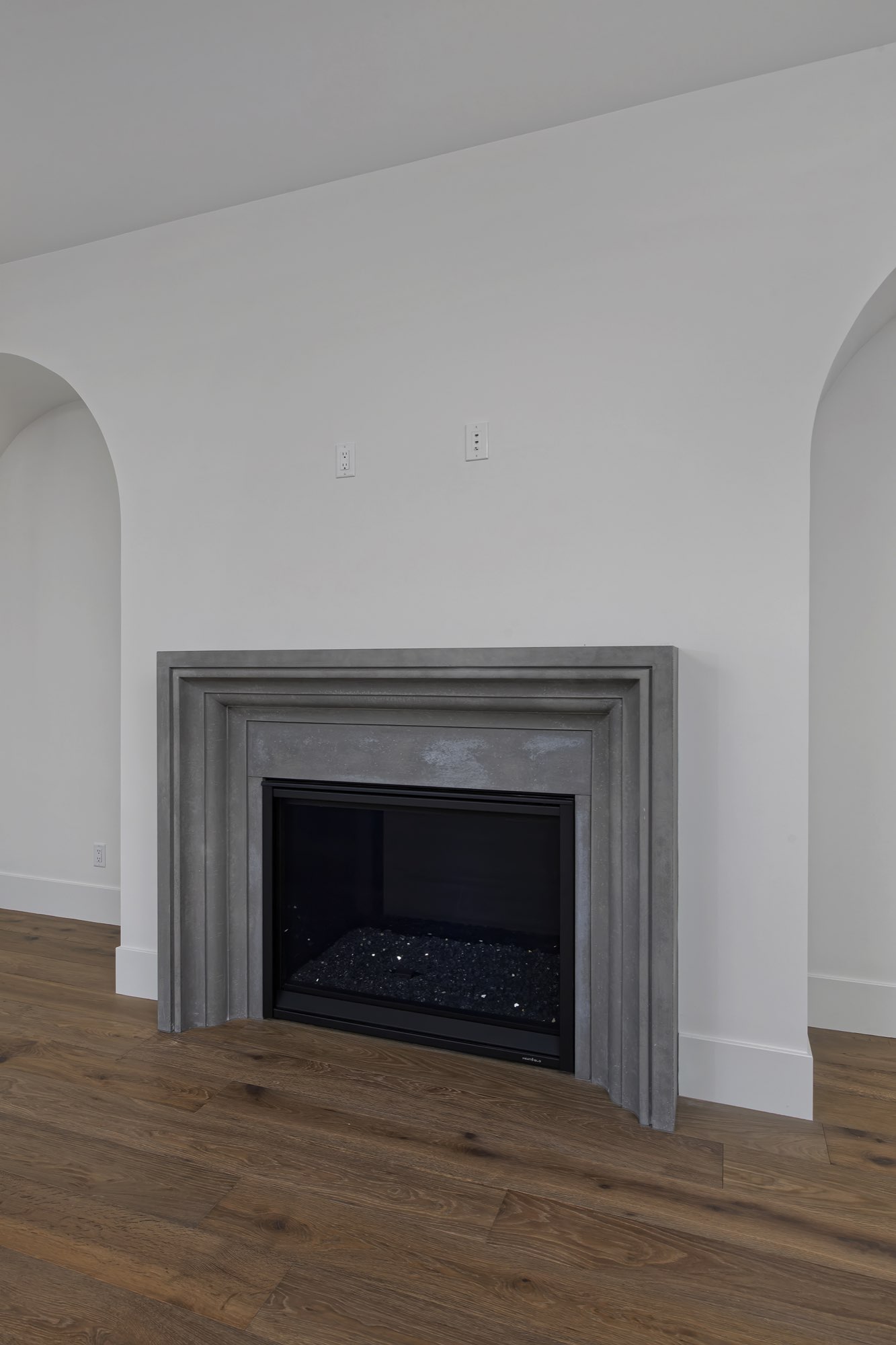 Close view of the gray fireplace surround with a black firebox and an arched niche