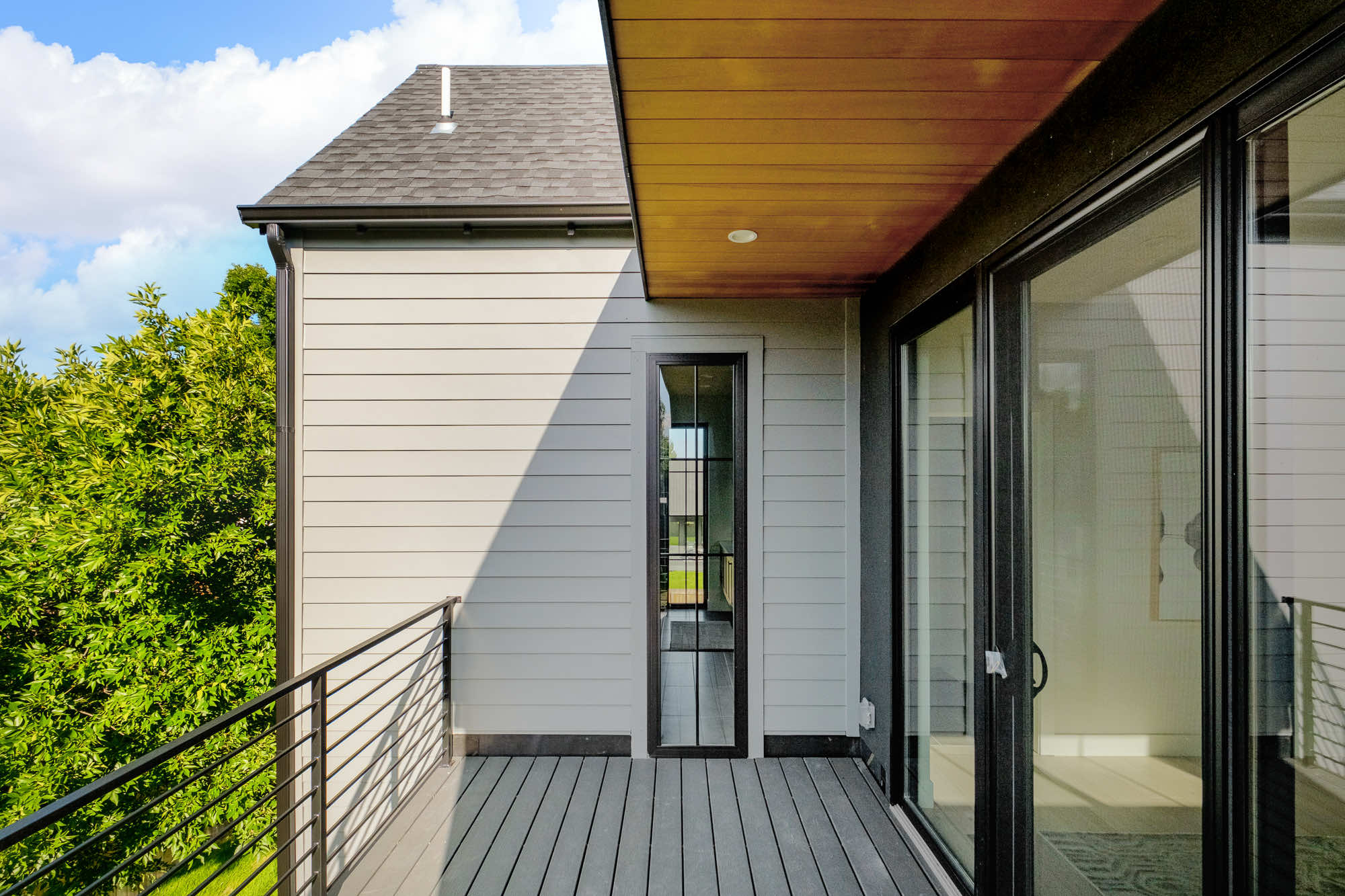 Balcony with a black horizontal railing, a wood-plank ceiling and the dark shingle roof above