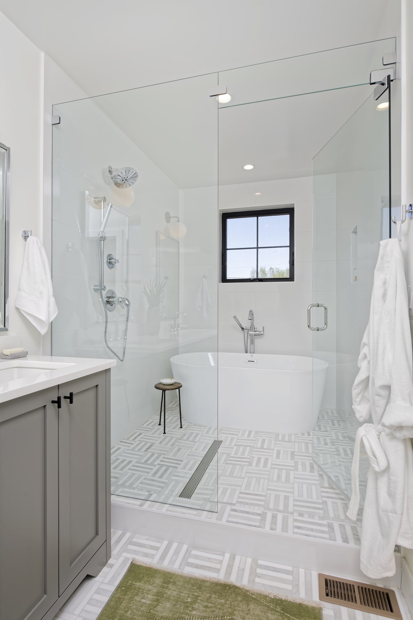 Glass-enclosed shower and freestanding tub with a patterned tile floor beside a gray vanity