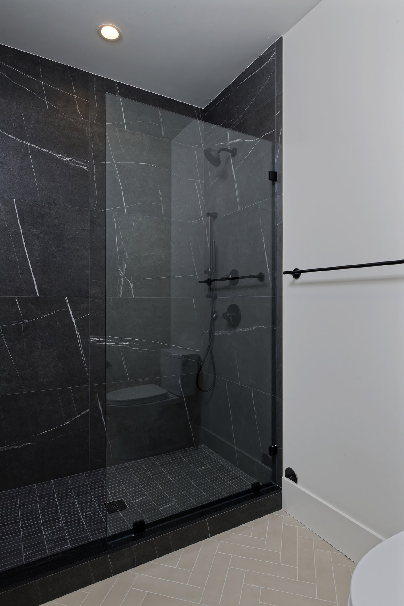 Walk-in shower in black stone-look tile with a glass door and herringbone floor